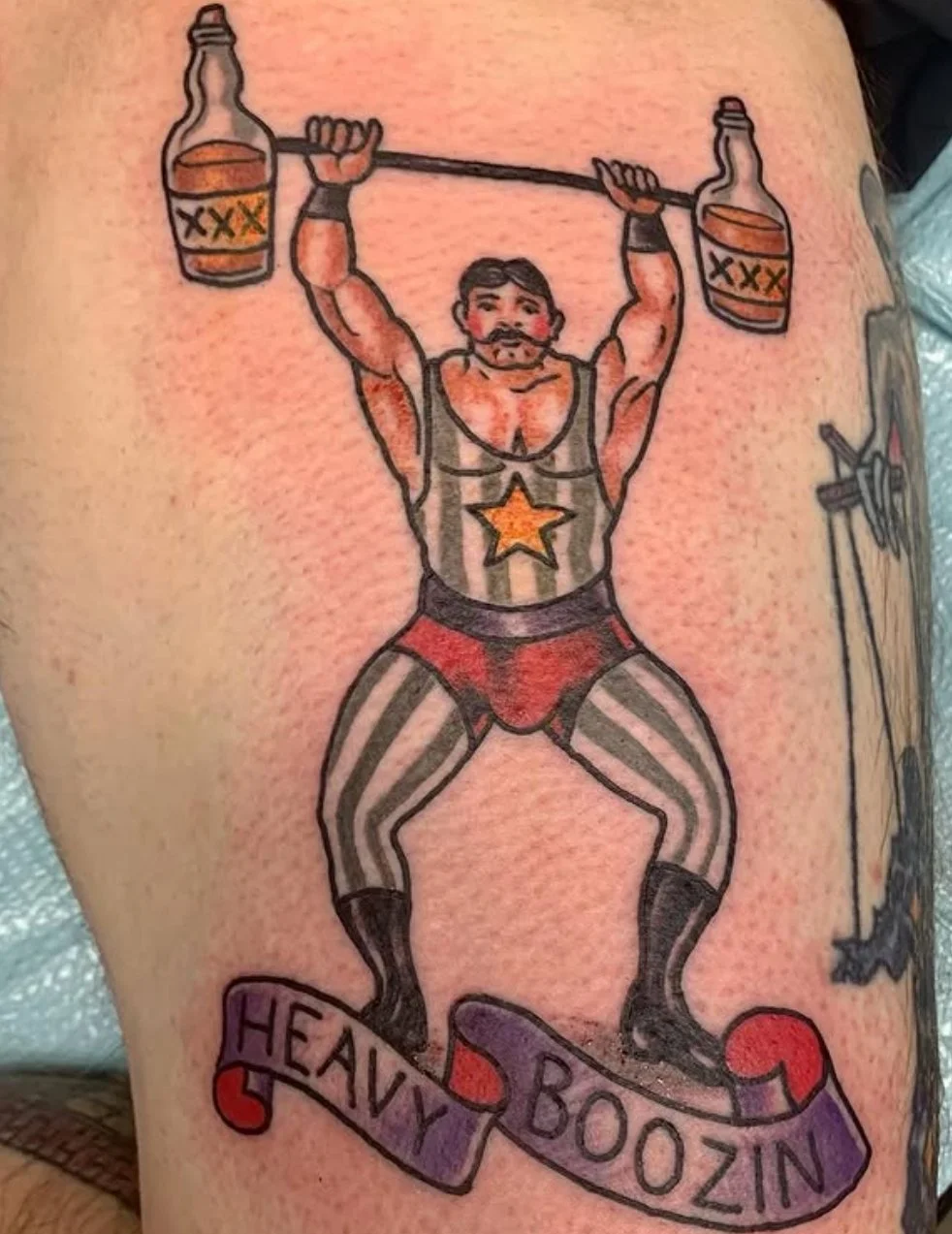 Tattoo of a muscular man lifting two bottles of alcohol as weights, wearing patriotic American-themed clothing with a star on his chest and striped leggings. Below, a banner reads "Heavy Boozin."