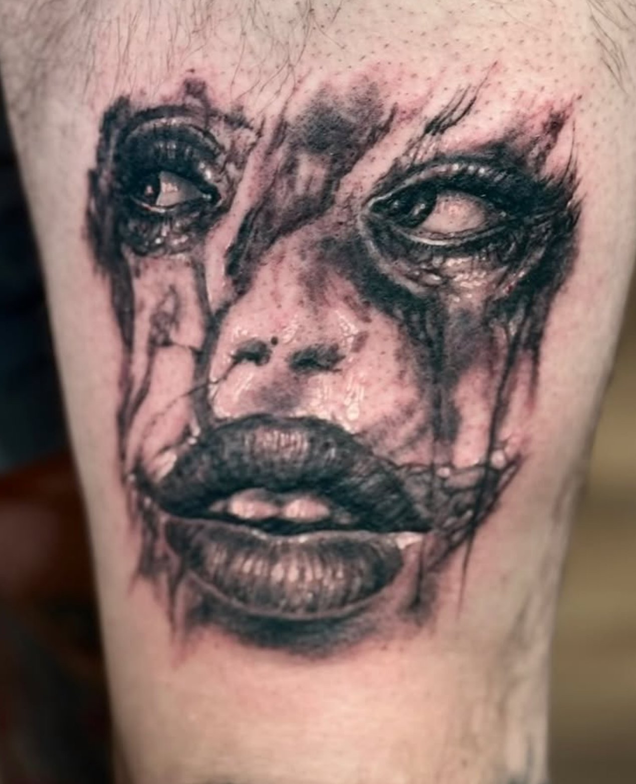 Tattoo of a woman's face with expressive eyes and lips, rendered in black ink with a sketch-like style.