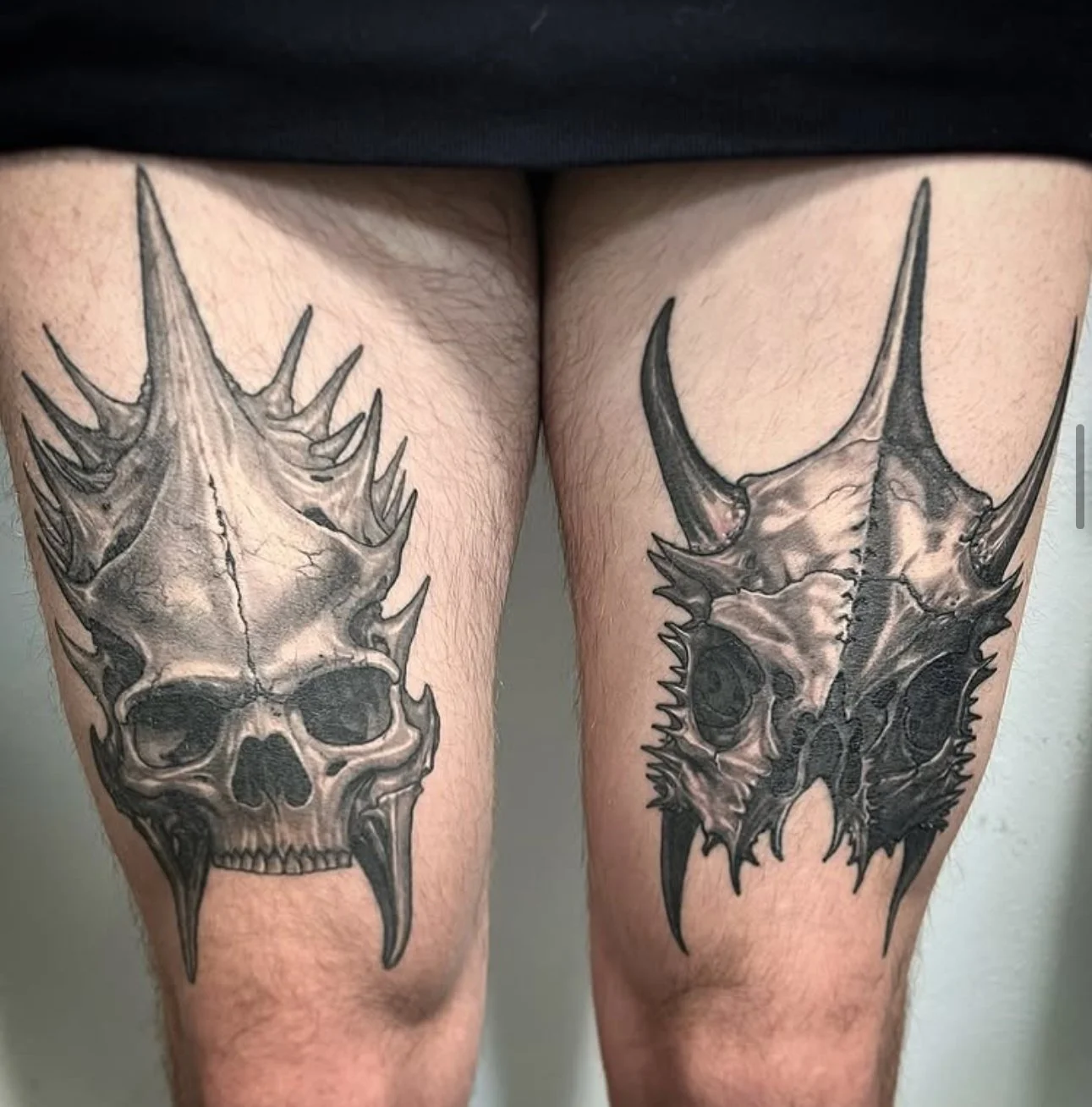 Black and gray tattoo of a skull with spiked and menacing features on the upper thighs.