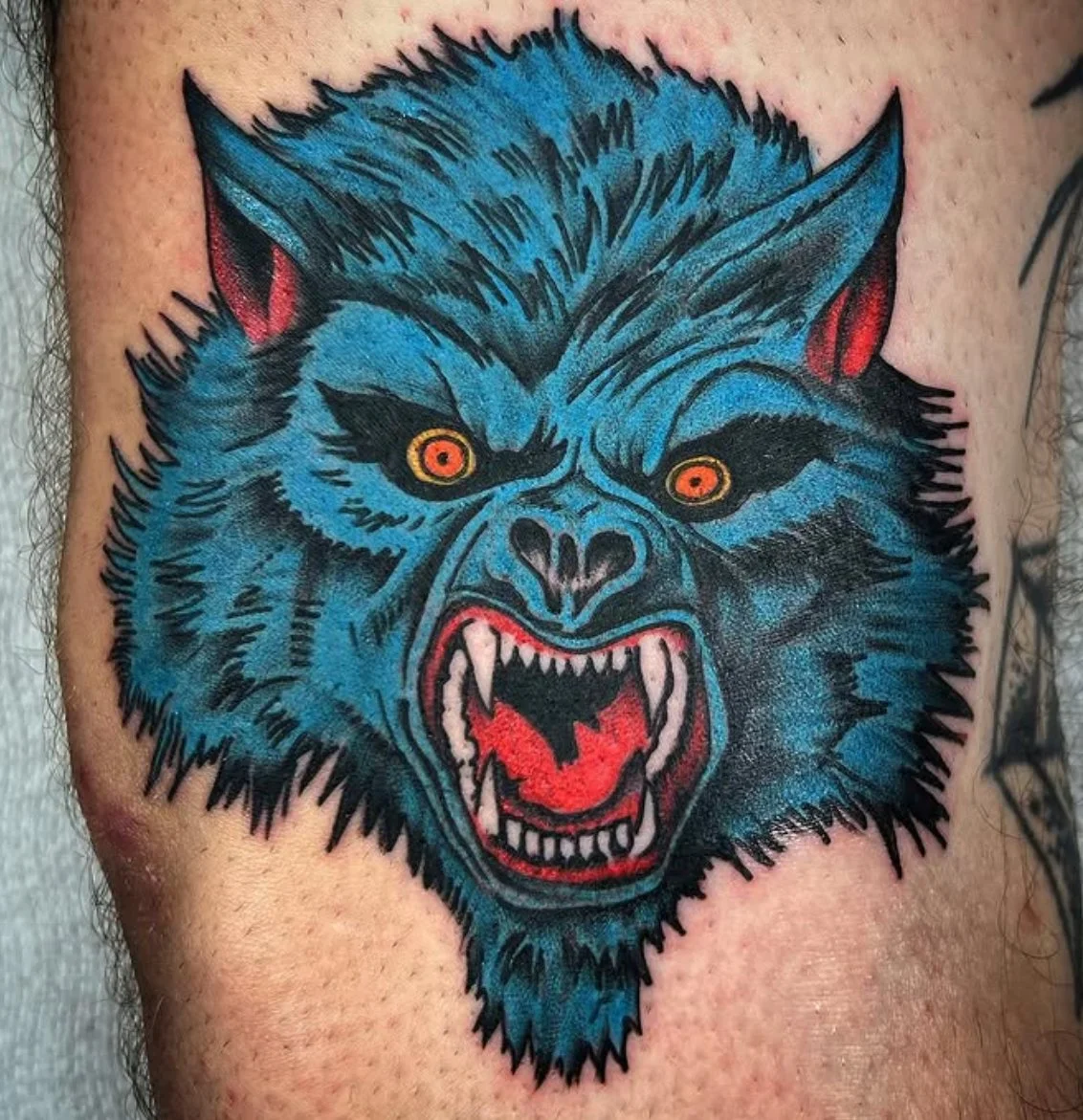 Tattoo of a fierce blue wolf with glowing yellow eyes, bared sharp teeth, and an angry expression.