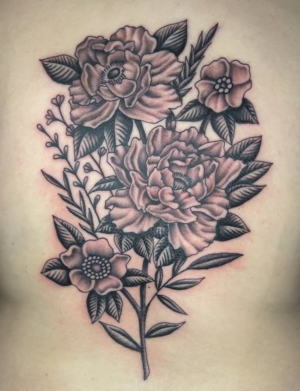 Black and gray tattoo of a bouquet of flowers on skin, featuring roses and other blossoms with detailed leaves.