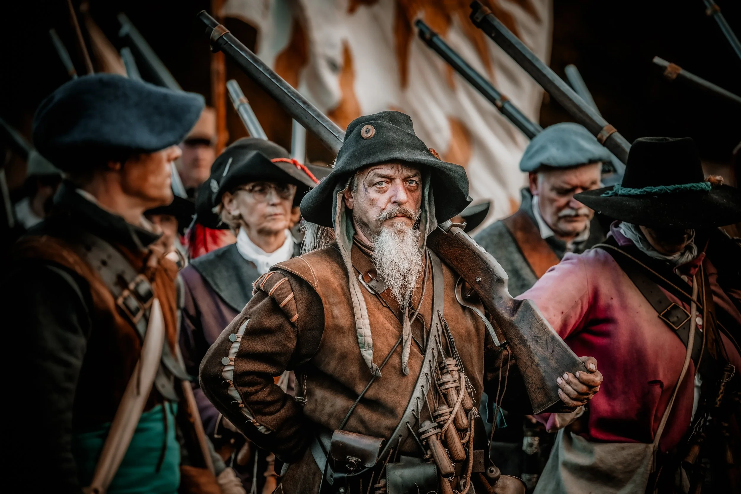 Mensen in middeleeuwse kostuums die een historische veldslag naspelen, met een man in het midden die een geweer draagt.