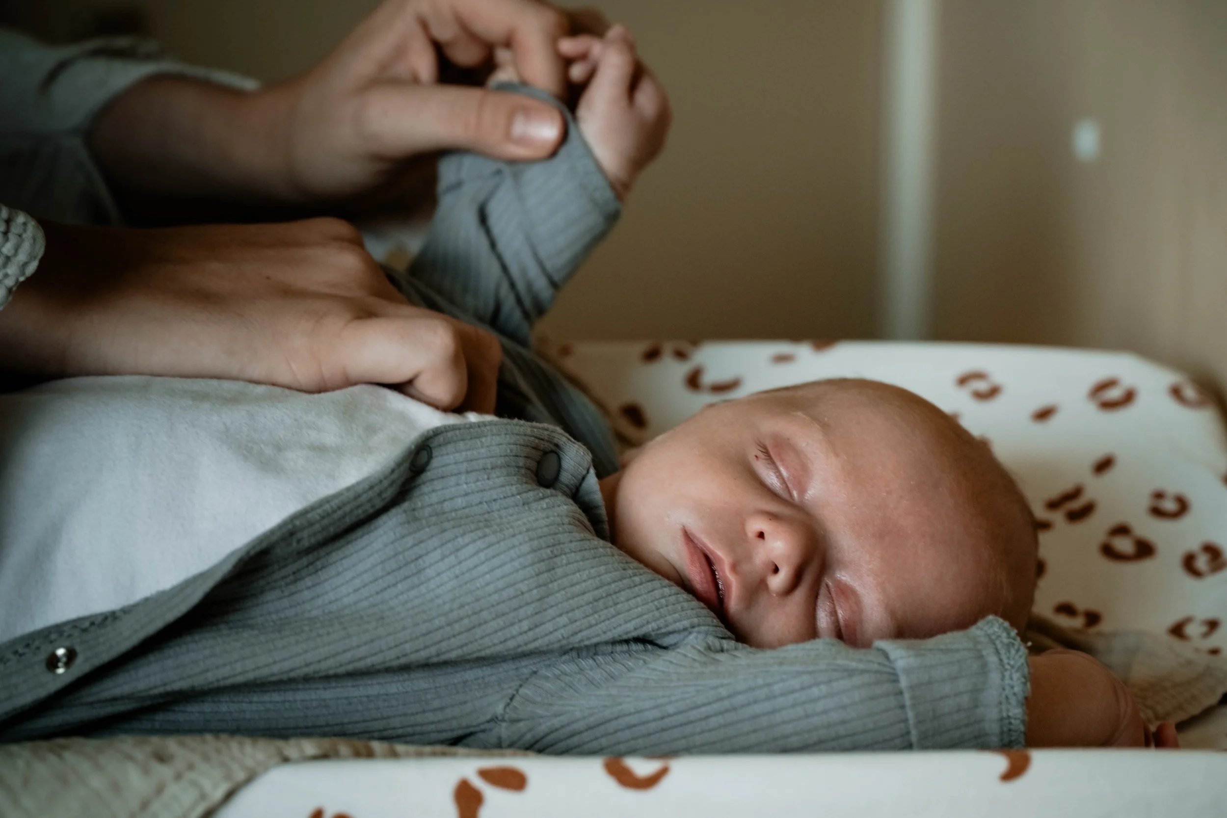 Een slapende baby ligt op een bed met een persoon die boven hem of haar een hand heeft.