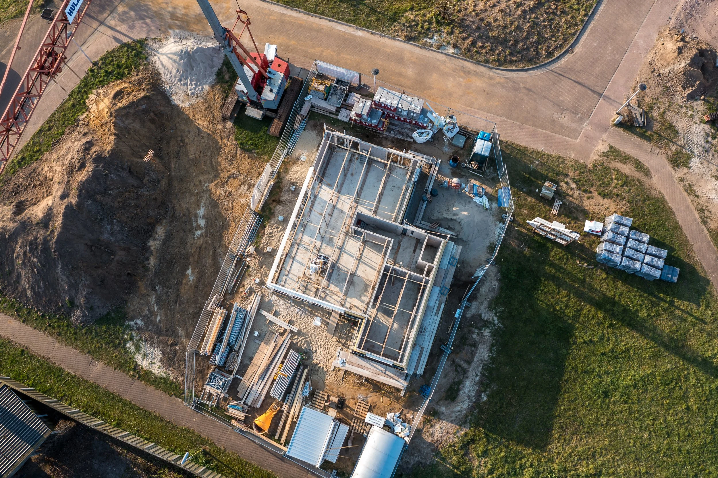 Bovenaanzicht van een bouwplaats met een onder constructie, bouwmaterialen en een hijskraan.