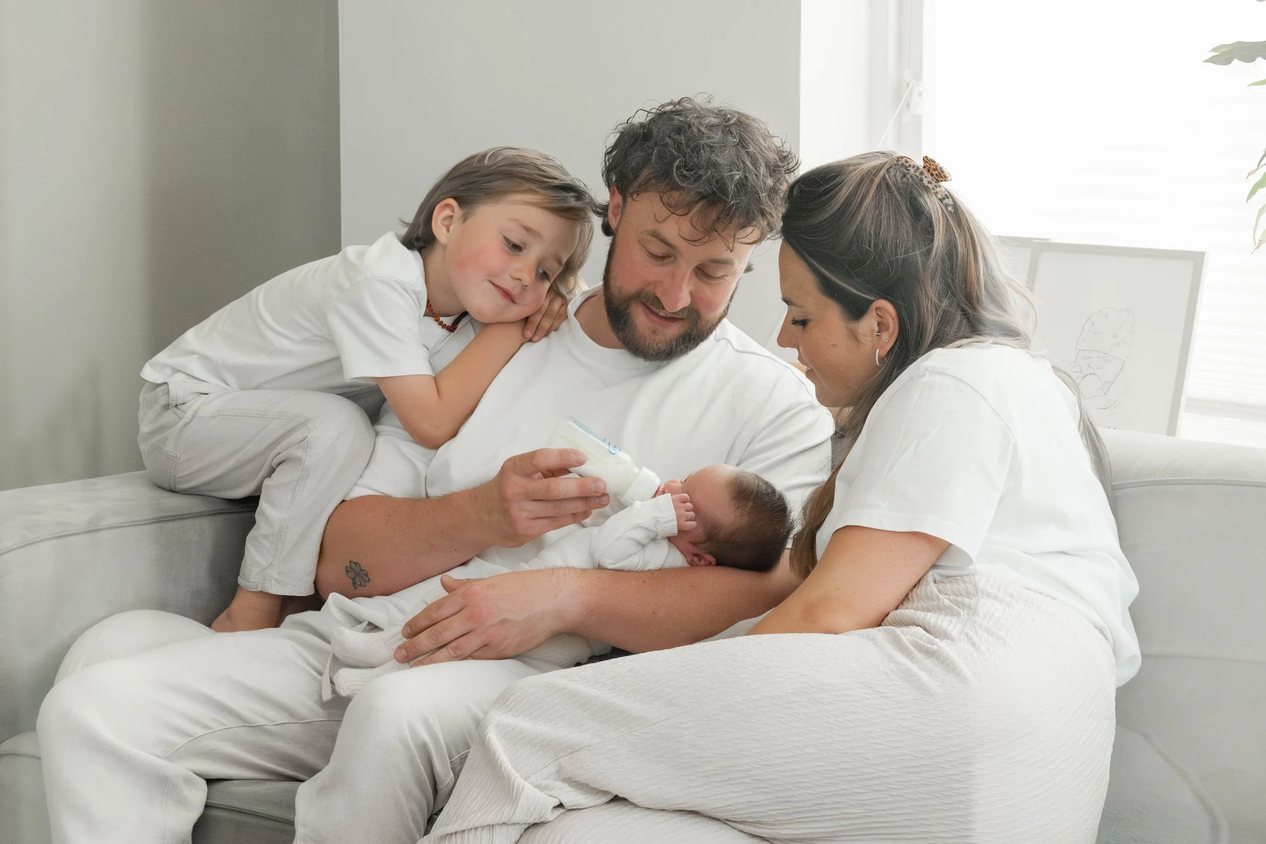 Familie met vader, moeder, een jongetje en een pasgeboren baby die flesje geven in een gezellige huiskamer