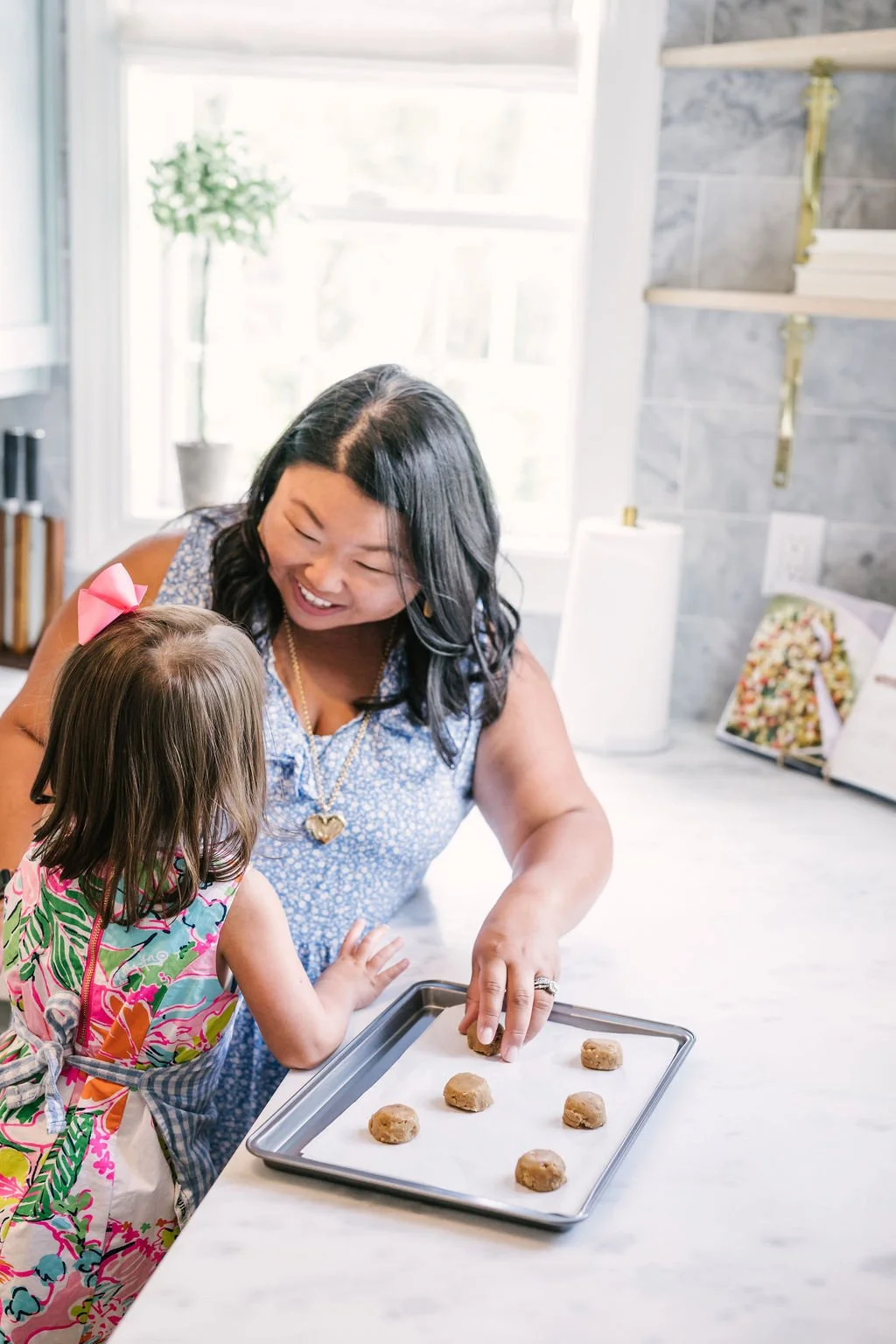 A woman and a young girl baking cookies together in a bright kitchen, smiling and sharing a joyful moment.