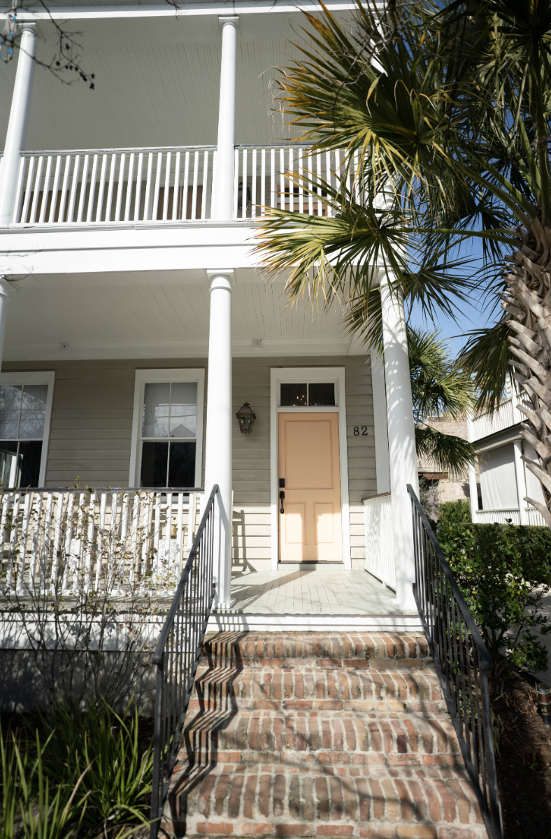 A modern wooden house located in a grassy field by a calm lake with mountains in the background at sunset.