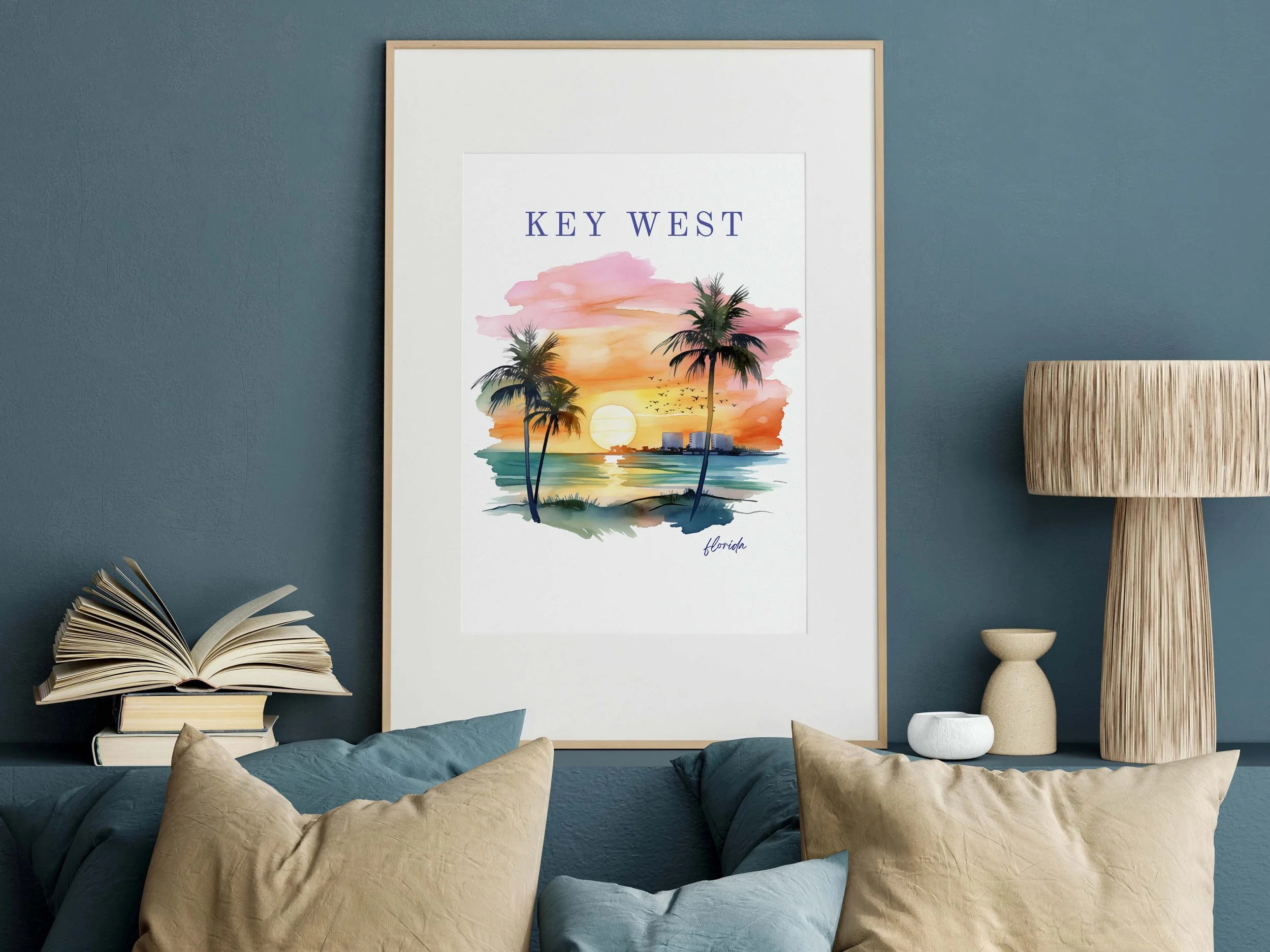 Decorative living room wall with a framed watercolor painting of a sunset with palm trees in Key West, Florida, and several cushions on a sofa.