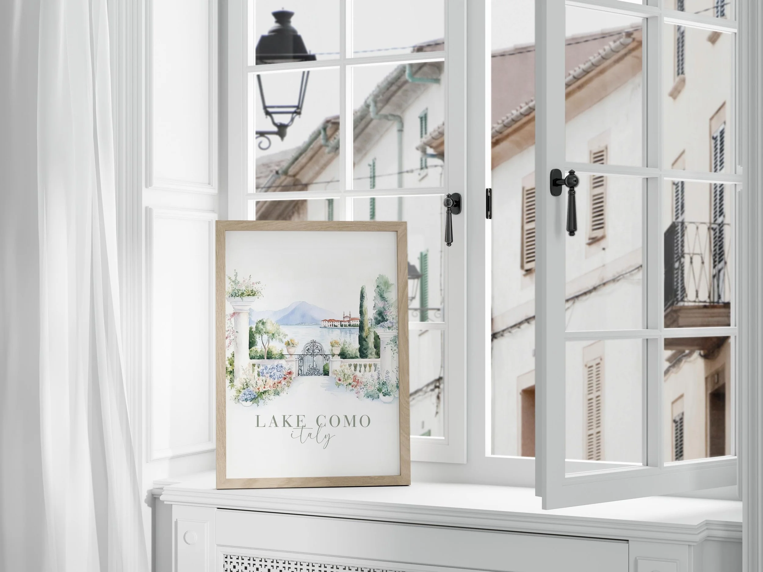 Watercolor painting of Lake Como, Italy, featuring a scenic view with a gated entrance, trees, mountains in the background, and the lake, placed on a windowsill with open window and white curtains.