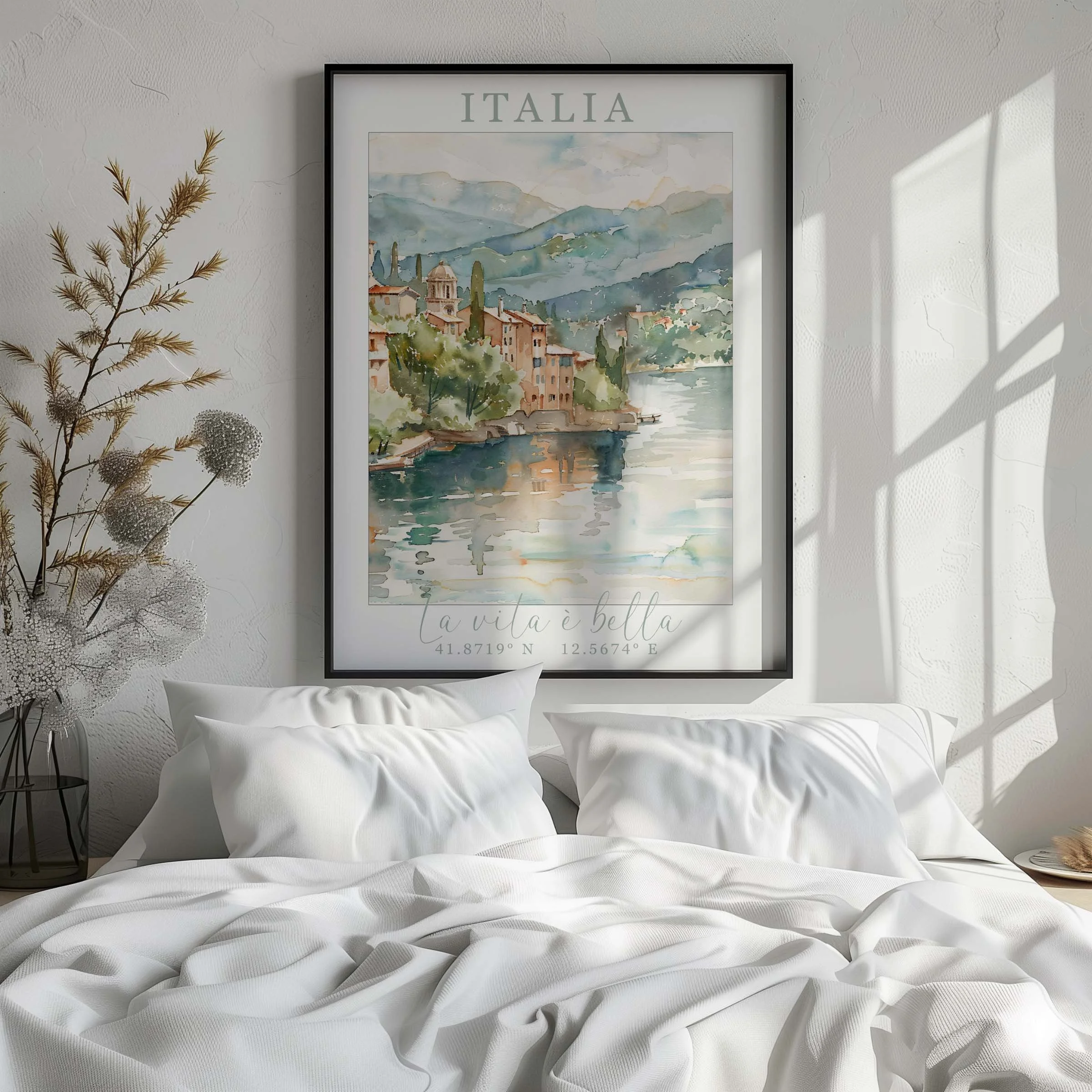 A cozy bedroom with white bedding and pillows, a large framed watercolor painting of an Italian lakeside scene on the wall, and natural sunlight casting shadows on the wall.