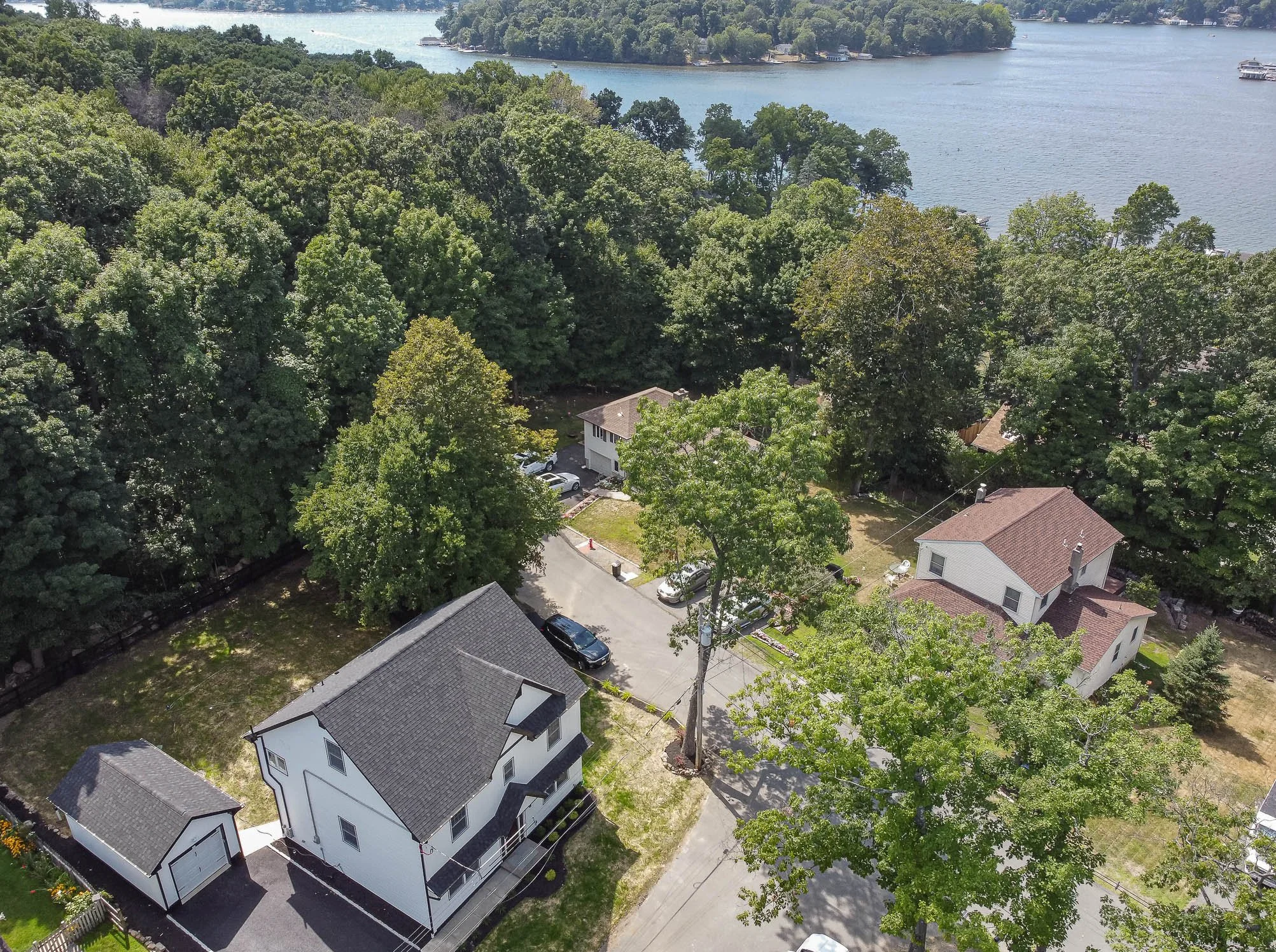 An aerial view of a neighborhood with houses, trees, and a body of water in the background, showing a mix of residential buildings and lush greenery.