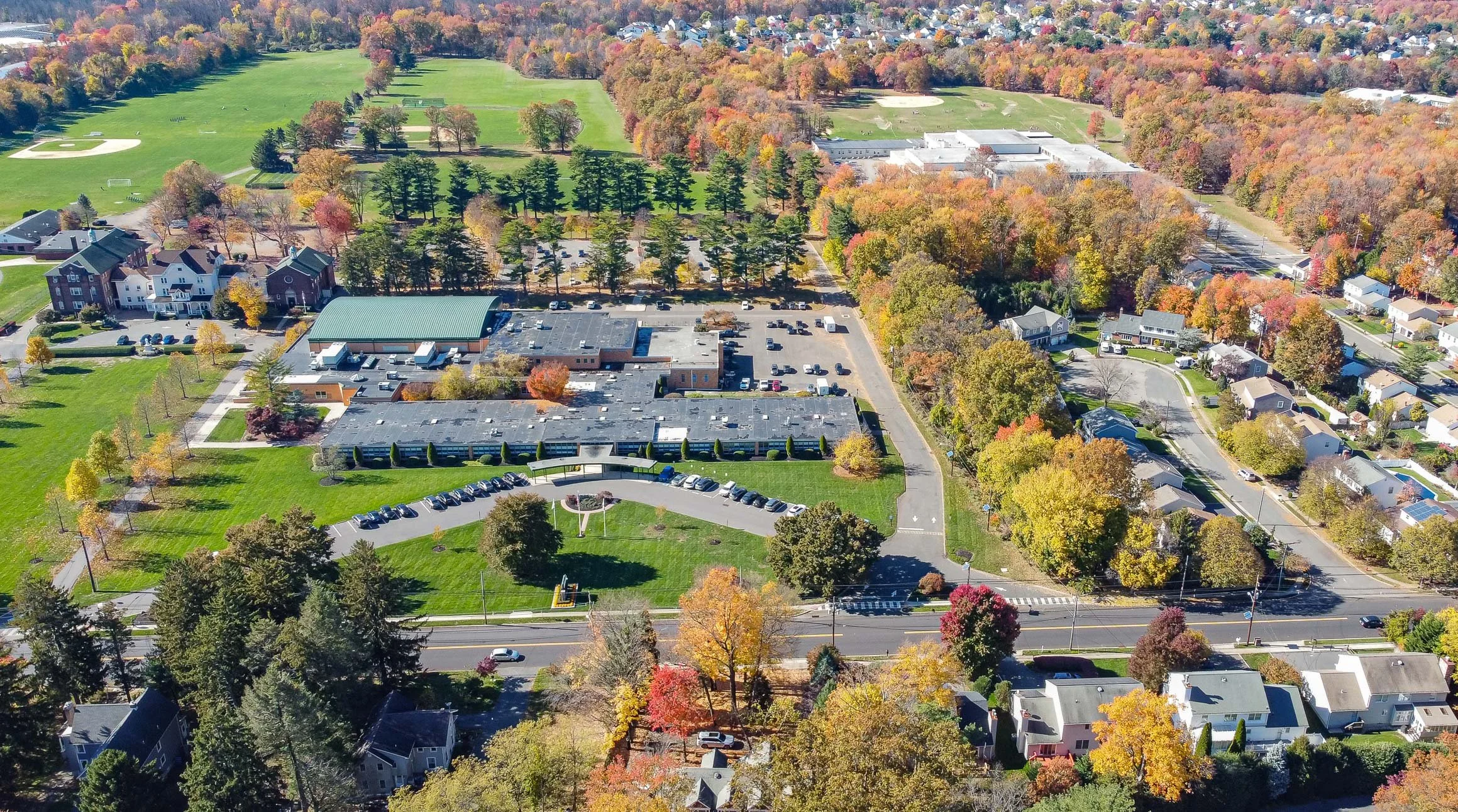 Aerial view of a neighborhood with a school and a park, surrounded by colorful autumn trees.