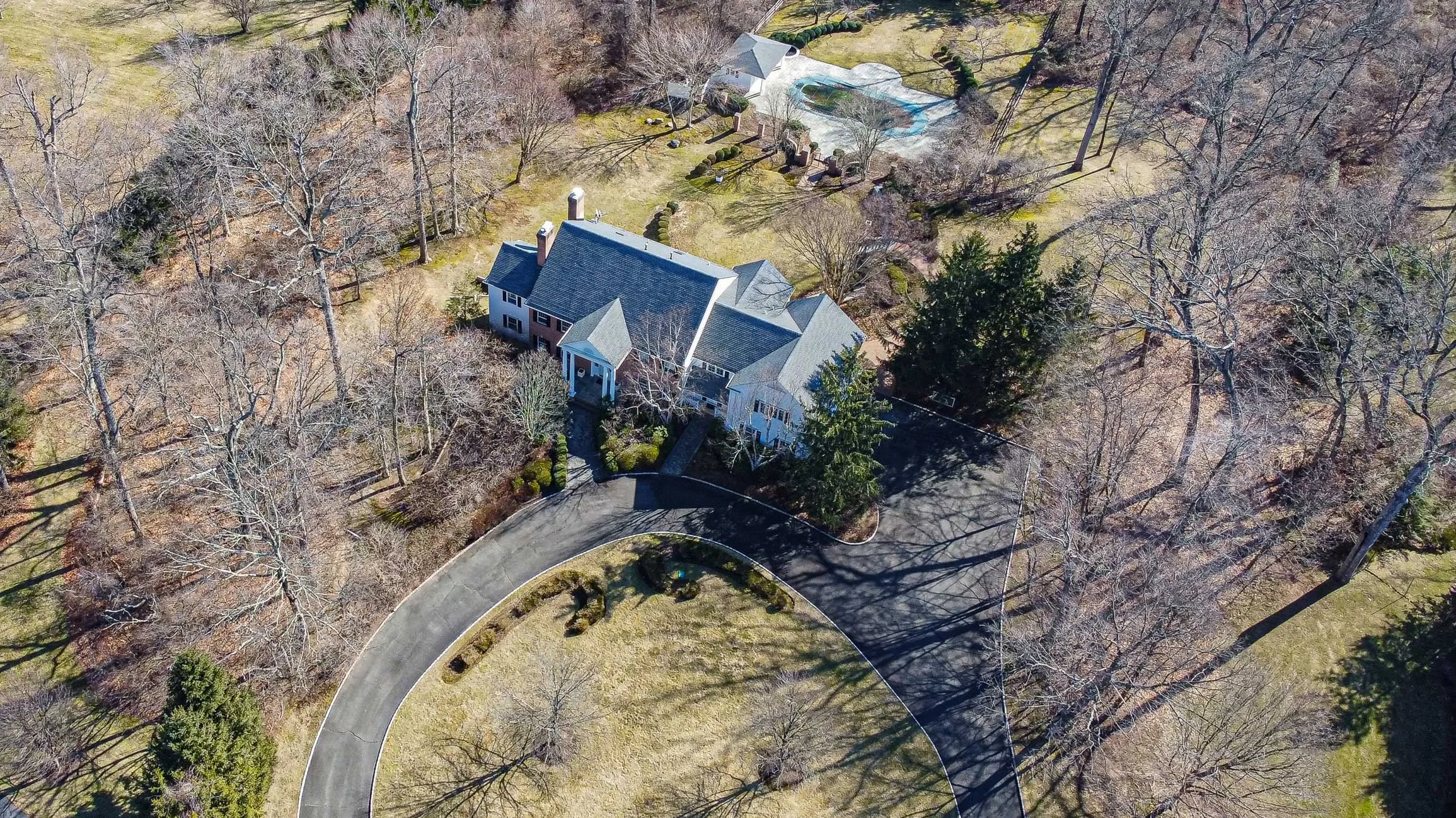 Aerial view of a large house with a circular driveway, surrounded by leafless trees and a grassy yard.