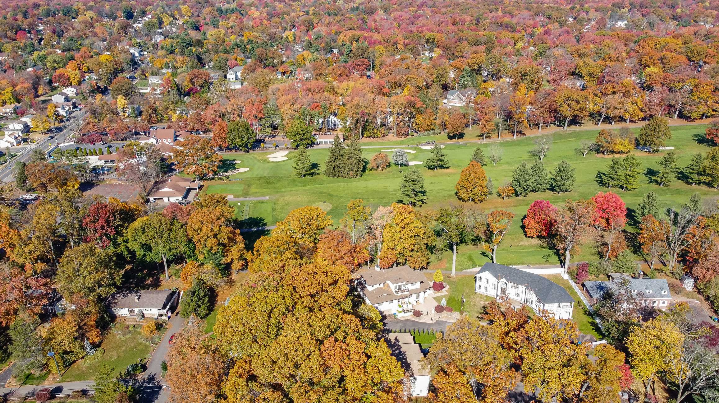 Aerial view of a suburban neighborhood with trees in fall colors surrounding a golf course.