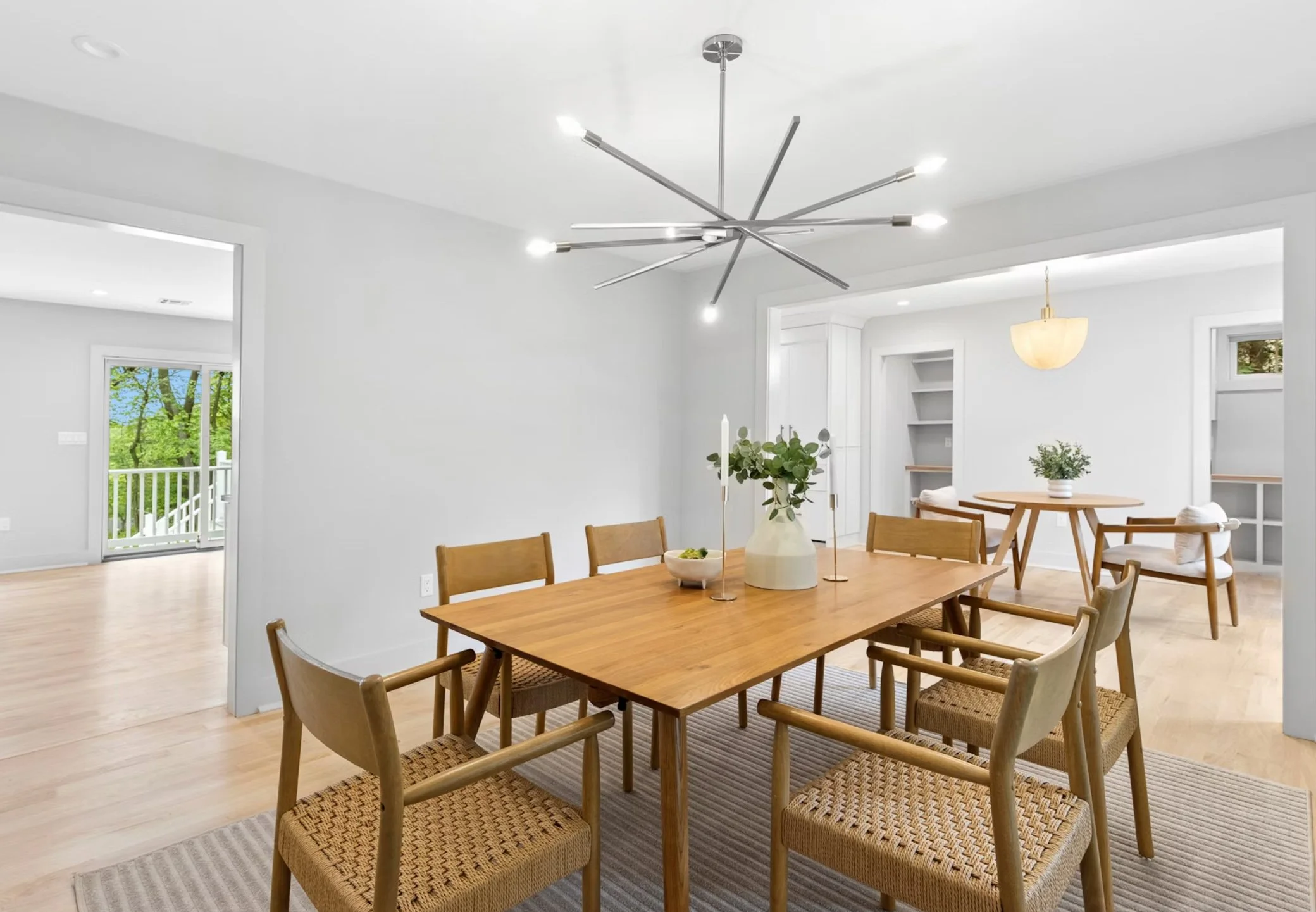 A modern dining room with a wooden table, six chairs, a decorative vase with greenery, and a light fixture on the ceiling.