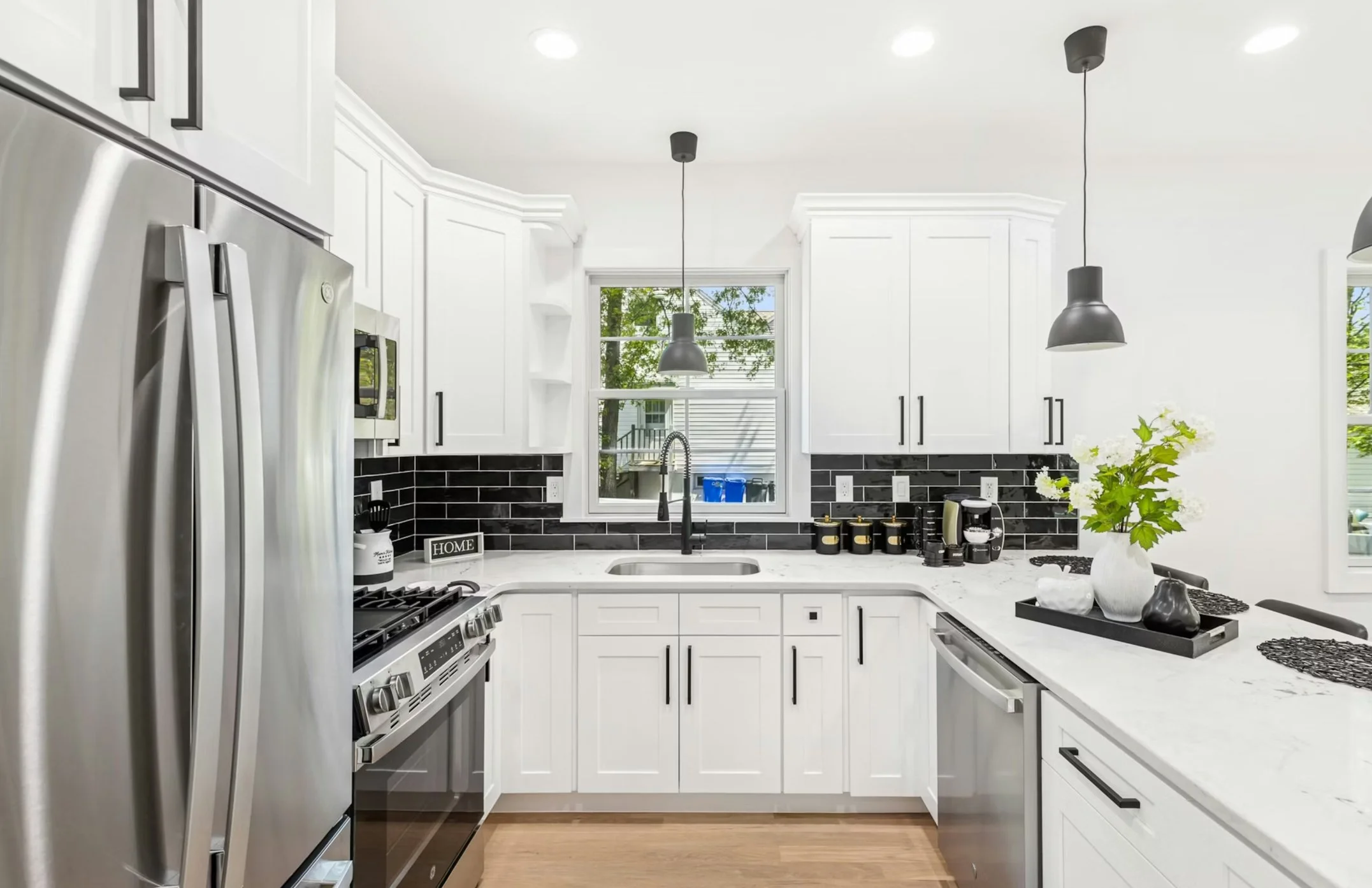 Modern white kitchen with black backsplash, stainless steel appliances, and decorative vases on the countertop near the window.