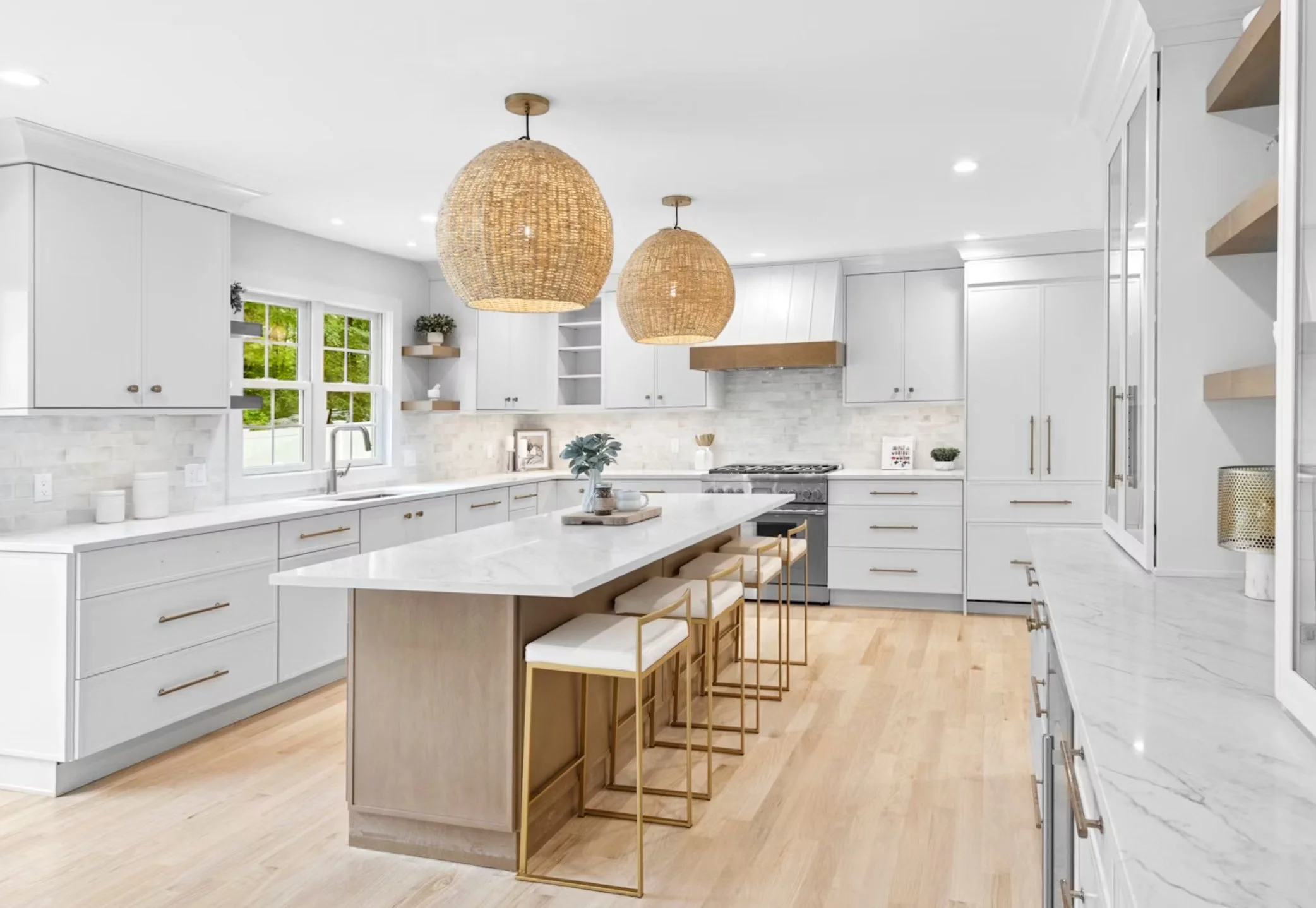 Modern white kitchen with wooden accents, large island with four bar stools, two woven pendant lights, and a window over the sink.