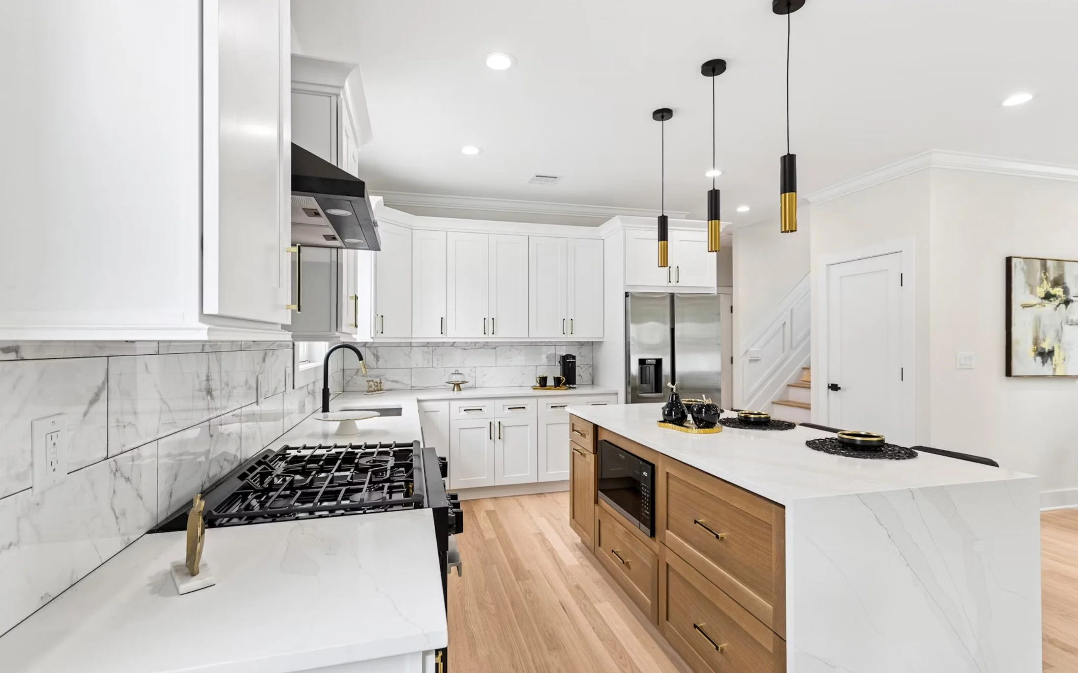 Modern kitchen with white cabinetry, marble backsplash, wooden island with built-in microwave, black pendant lights, stainless steel refrigerator, and hardwood floors.