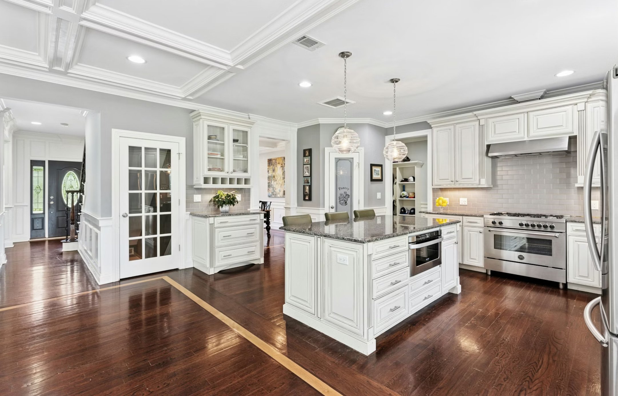 Bright kitchen with white cabinets, dark granite island, stainless steel appliances, and hardwood floors.