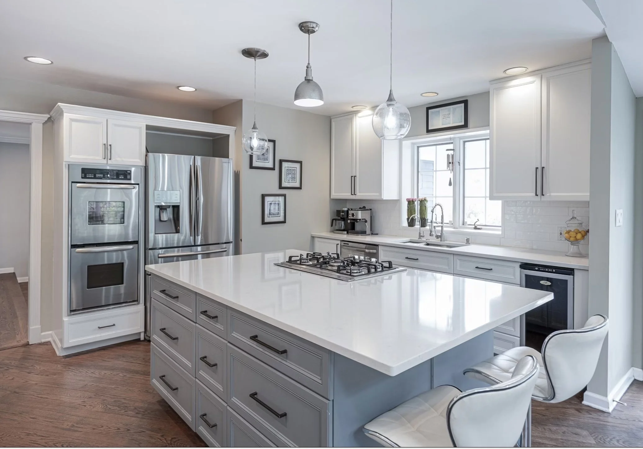 Modern kitchen with white cabinets, large island with white countertop, stainless steel appliances, and hardwood floors.