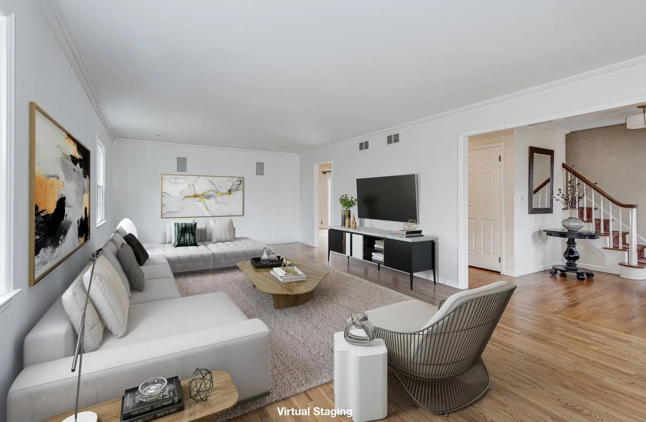 Living room with white walls, hardwood floors, a large white sofa with throw pillows, a modern armchair, a wooden coffee table, artwork on the walls, and a large flat-screen TV on a black TV stand.
