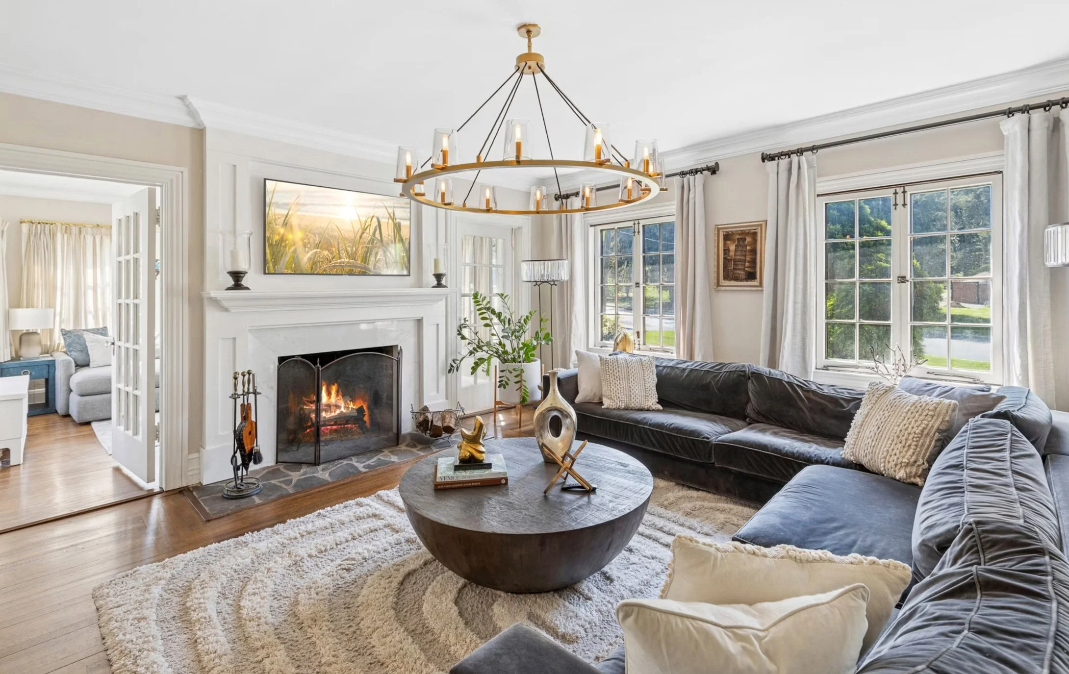 Living room with a fireplace, black sectional sofa, round coffee table, and large windows with white curtains.