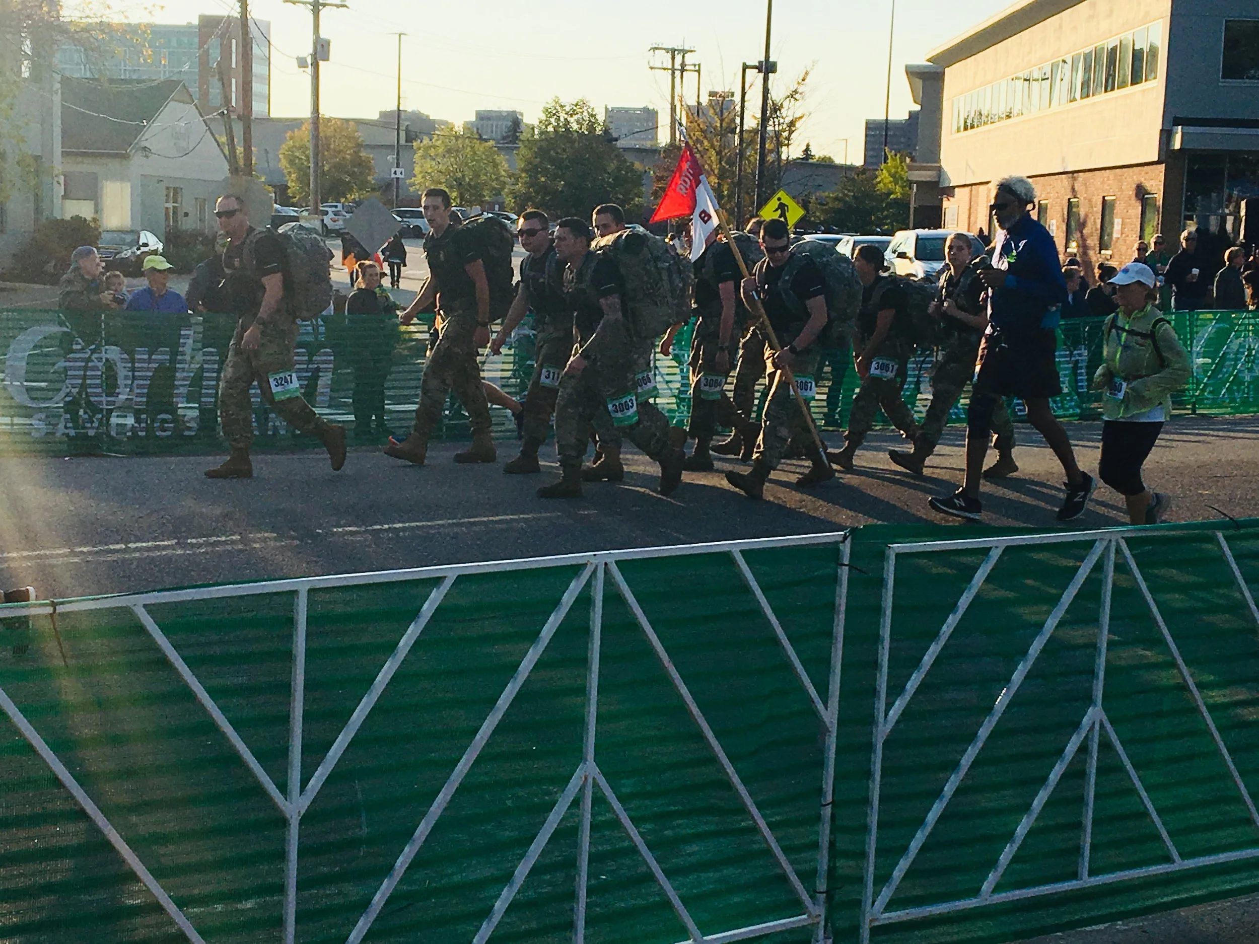 Group of people walking in a marathon event with some carrying backpacks and a flag.