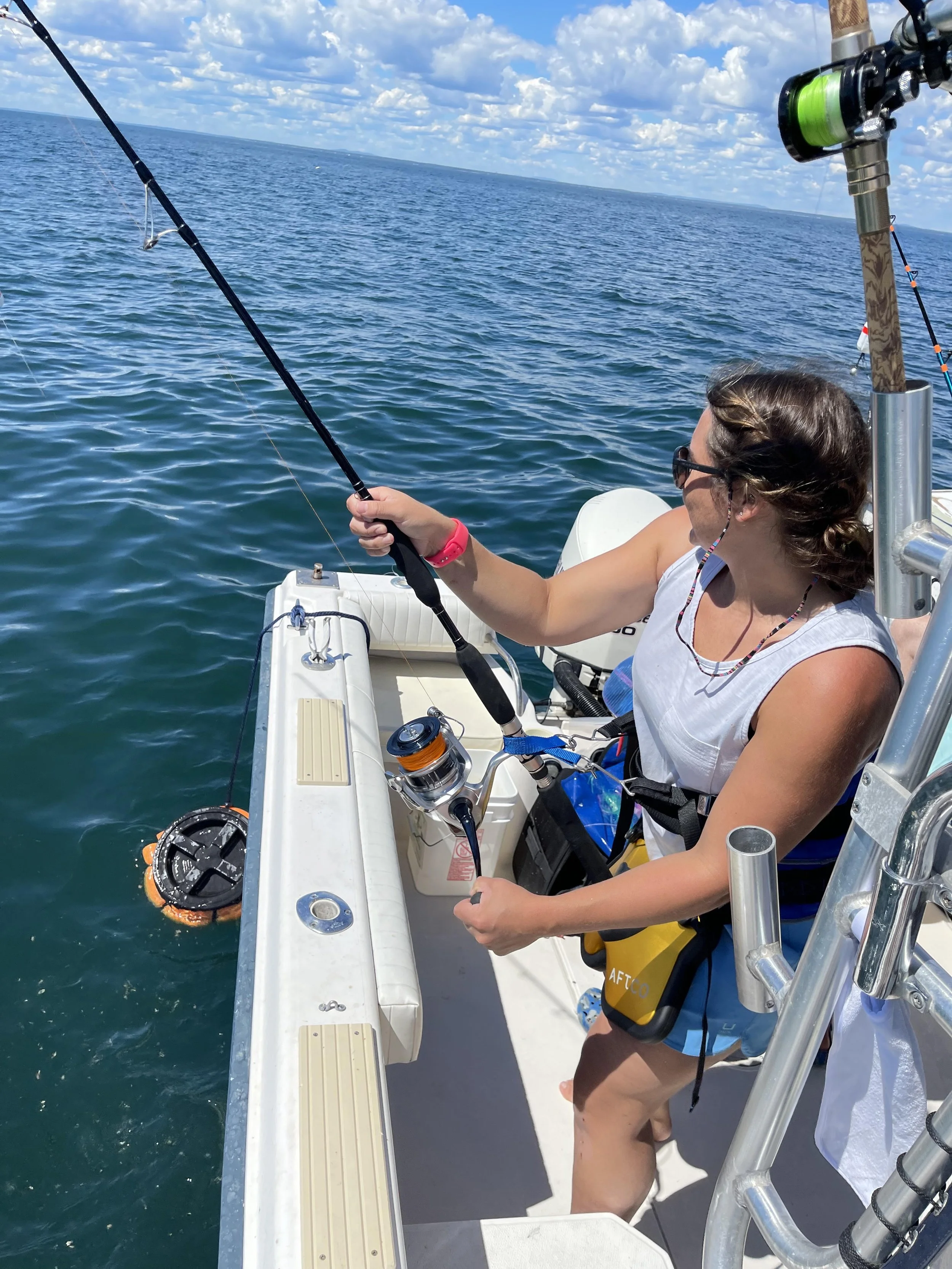 Person fishing from a boat on a sunny day with blue sky and water.