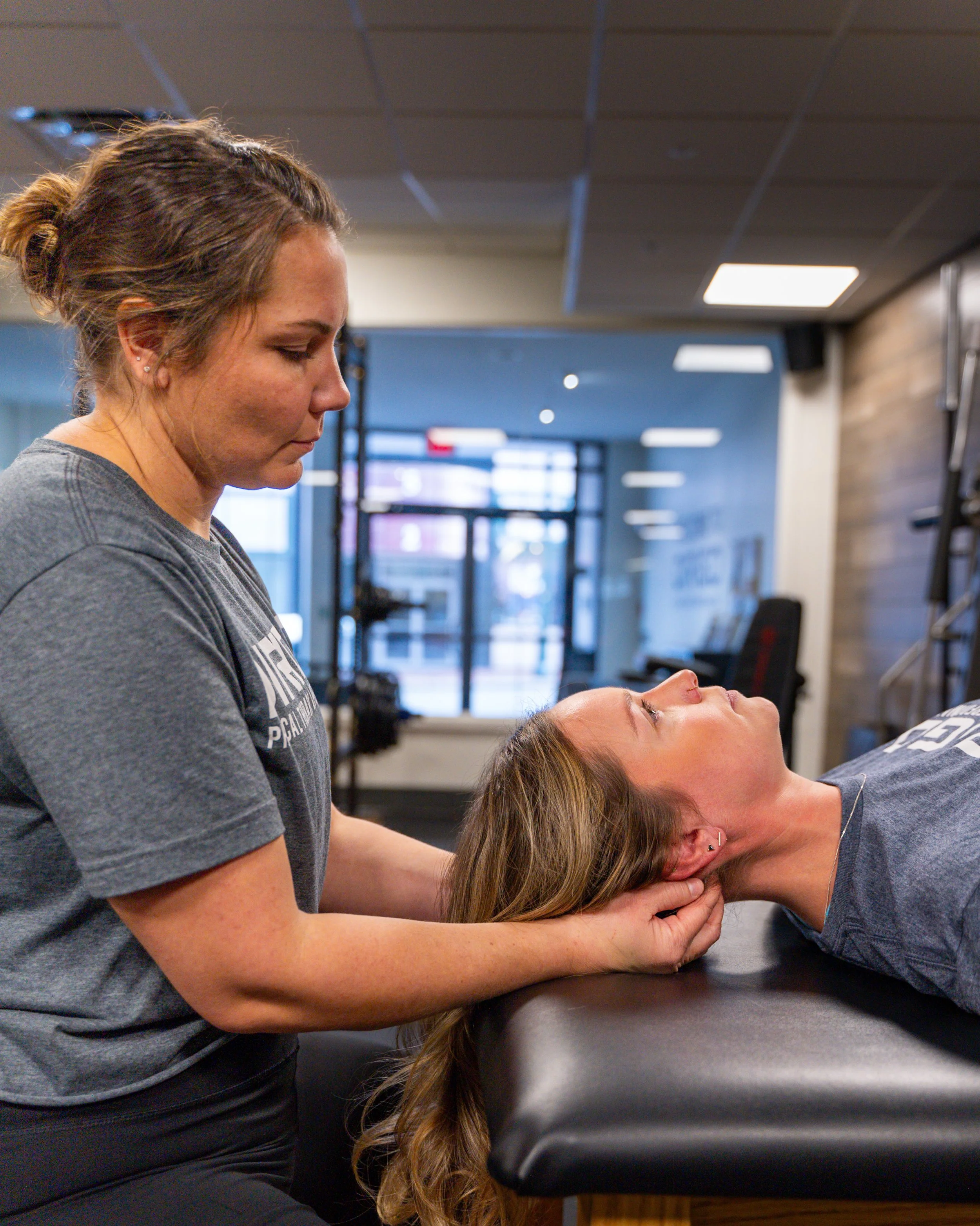 A physical therapist performs neck therapy on a woman lying on a table in a clinic setting.