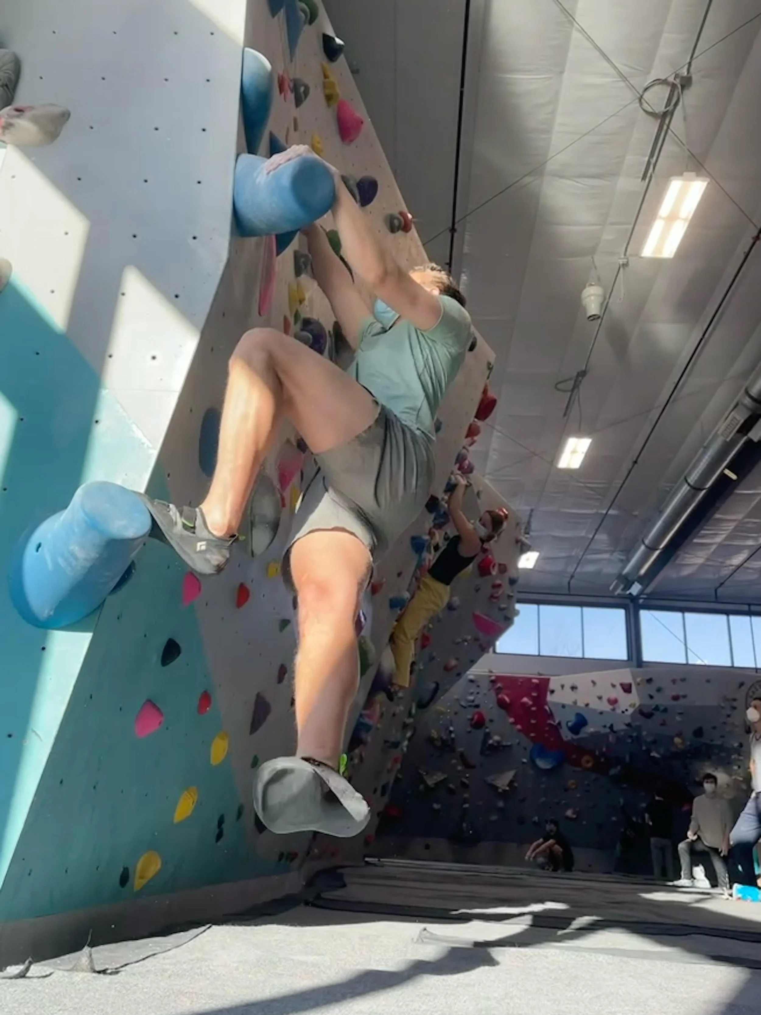 Person bouldering on an indoor climbing wall with colorful holds