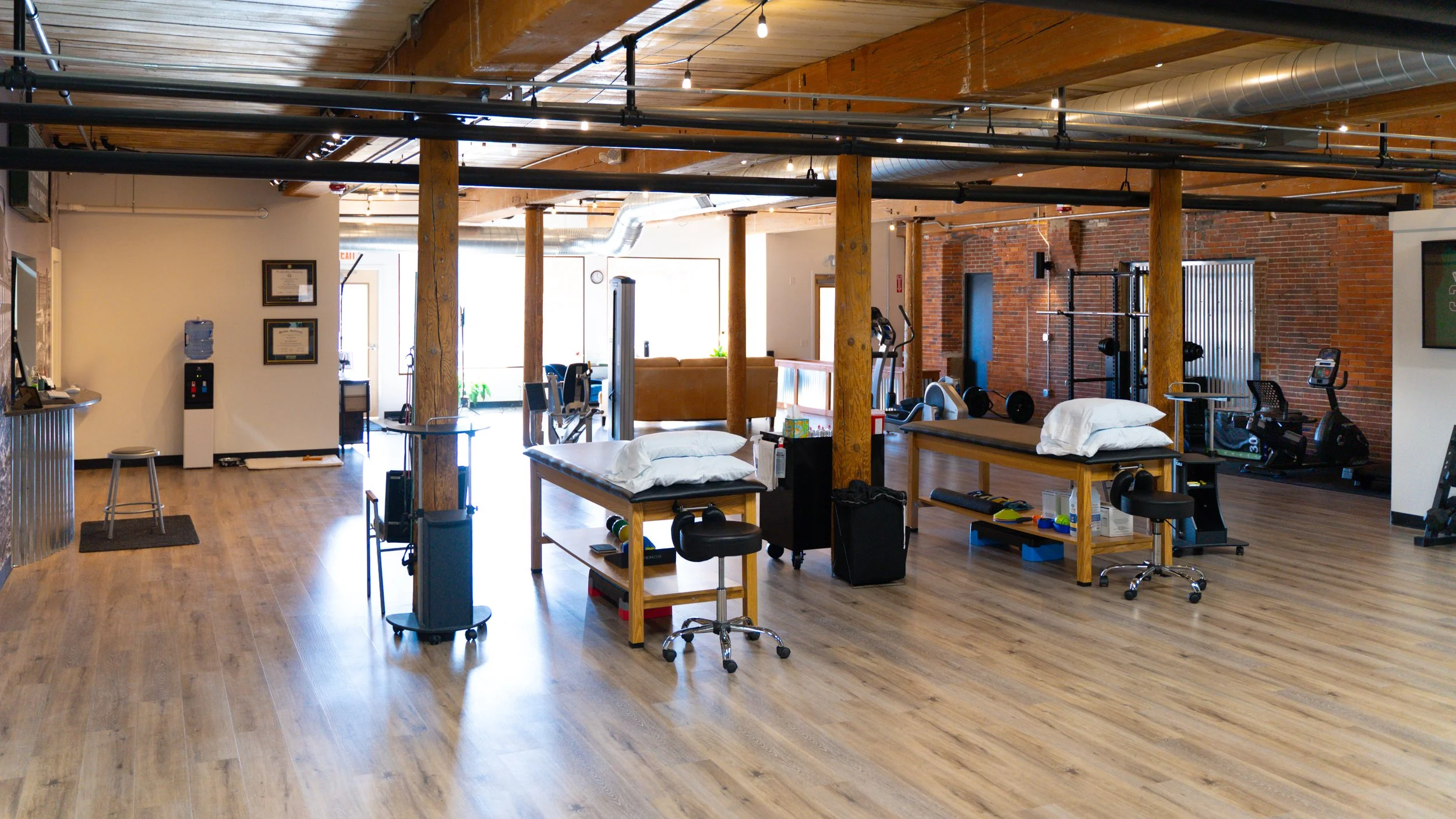Interior of a modern gym with treatment tables, exercise equipment, and wooden beams, featuring a bright and open design.