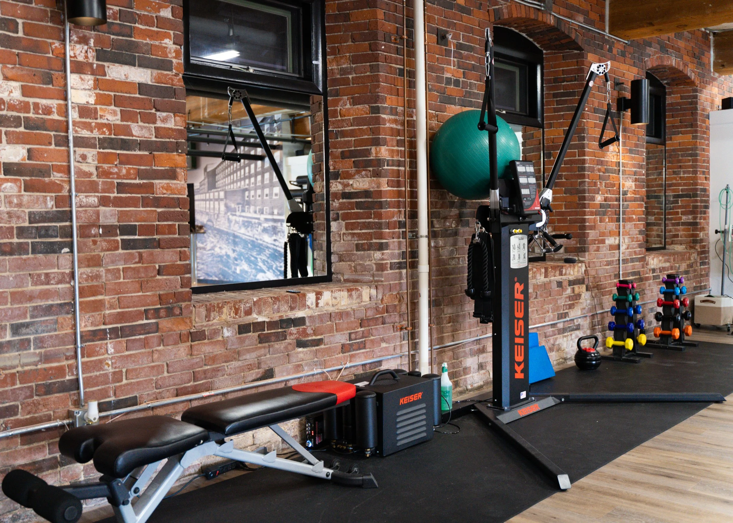 Indoor gym with exercise bench, Keiser equipment, exercise ball, and dumbbells.