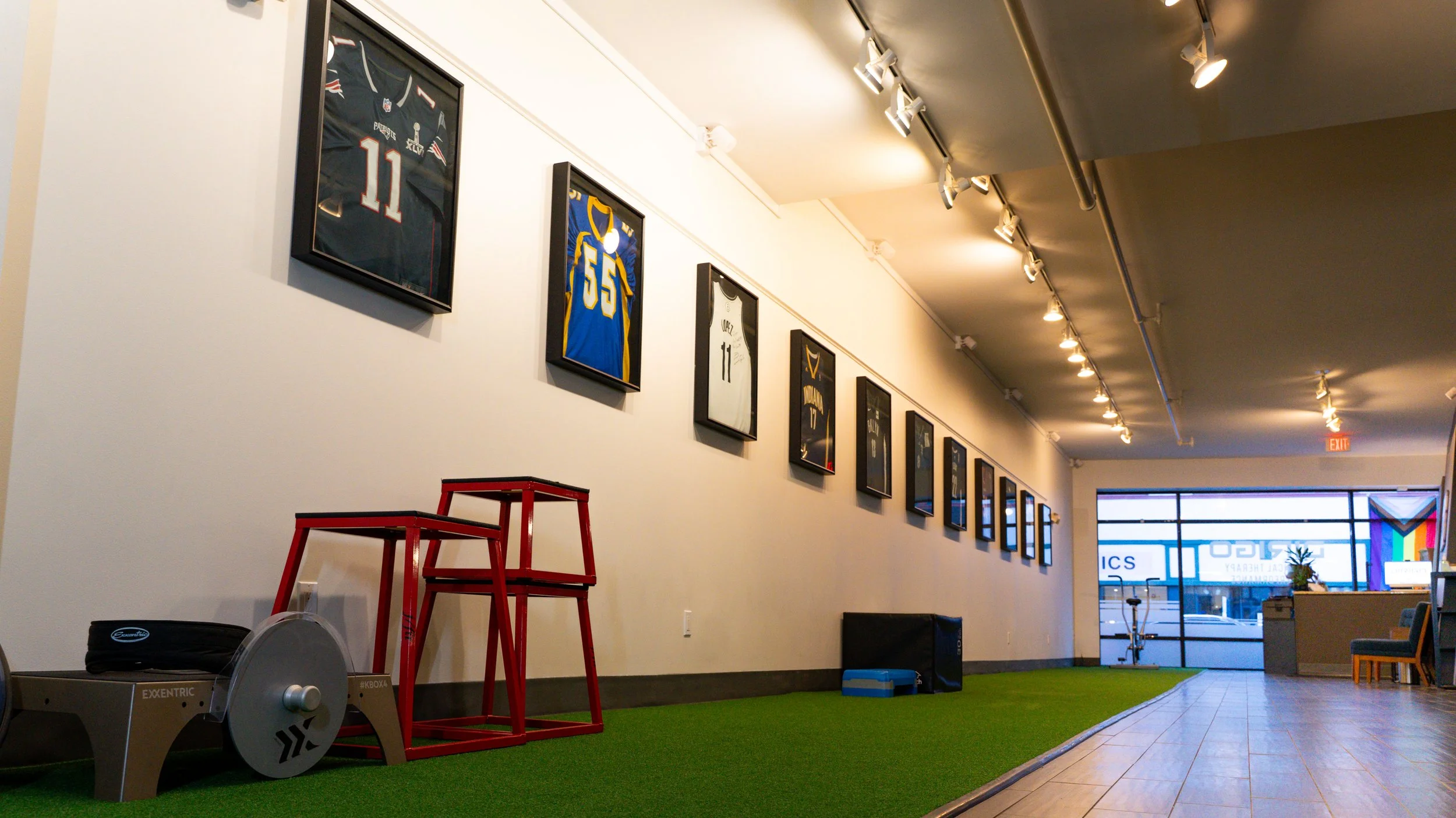 Framed sports jerseys on a gym wall with exercise equipment on a green turf floor.