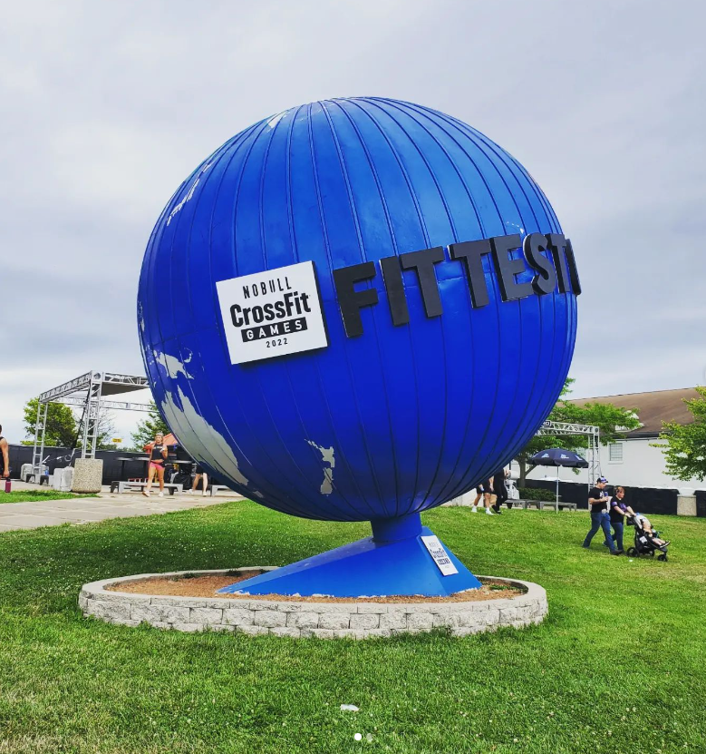 Large blue globe sculpture with "Fittest" and "CrossFit Games 2022" sign outdoors on grass