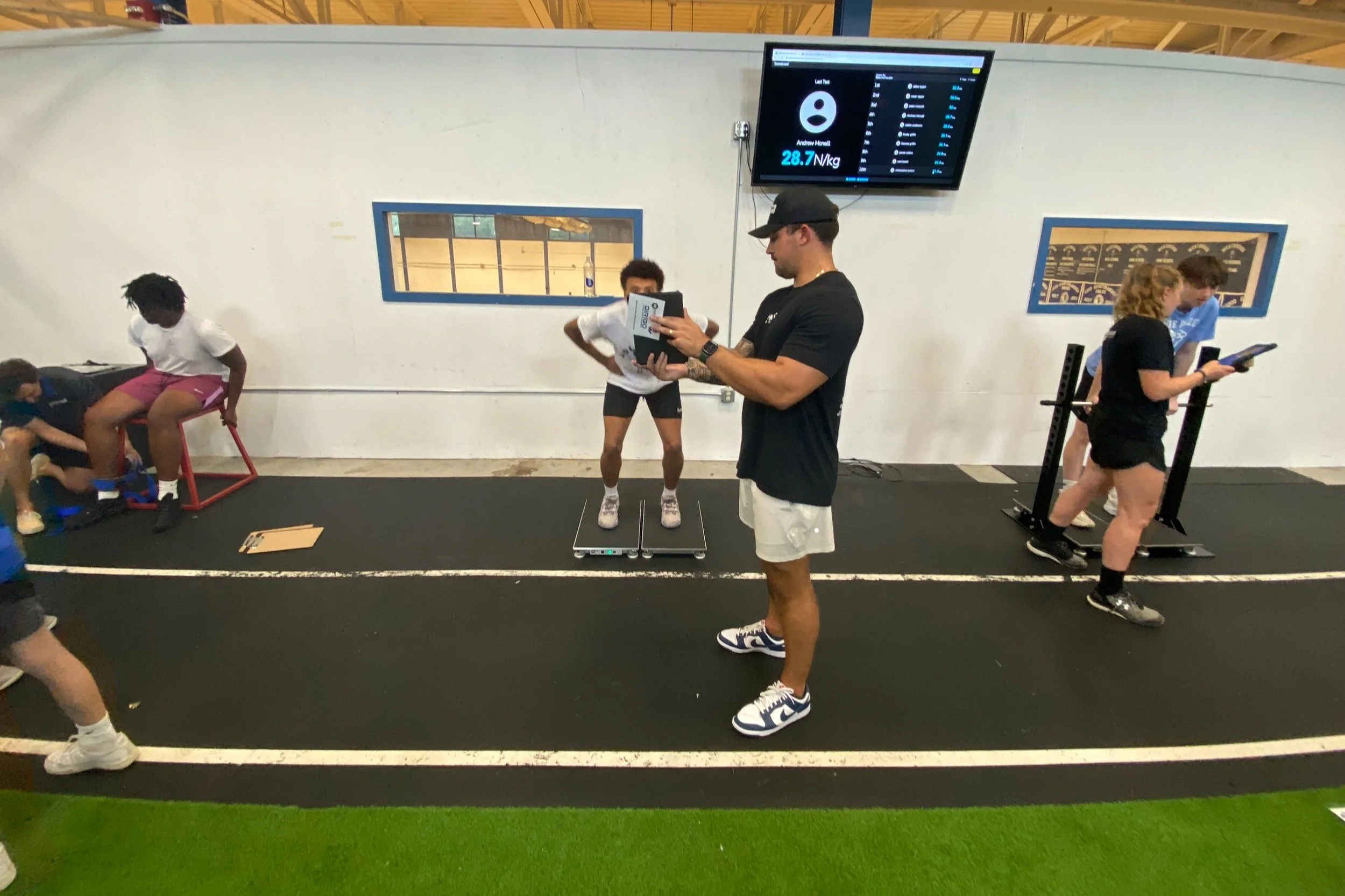 Gym training session with people exercising, using equipment, and monitoring results on a screen.