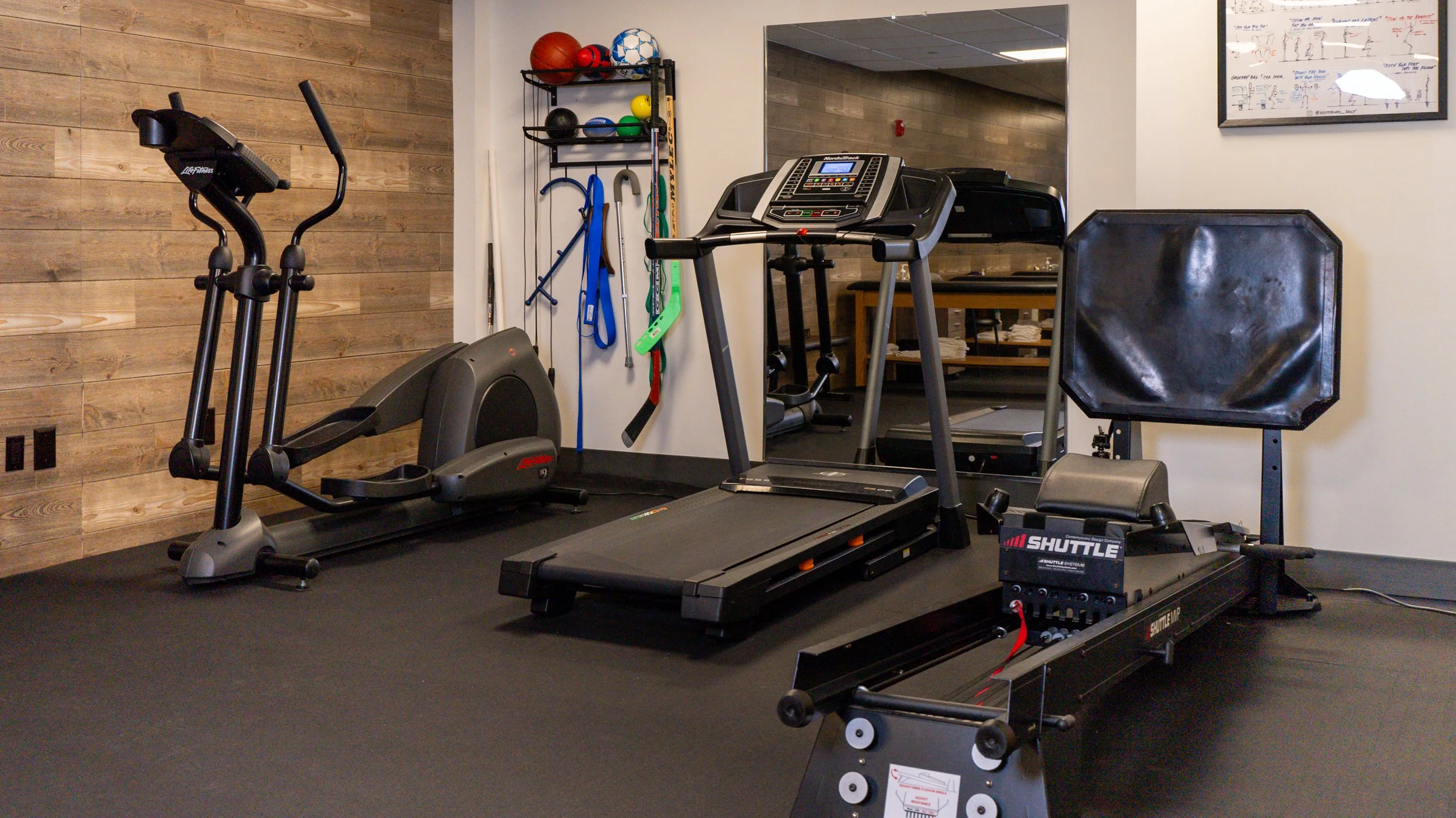 Home gym with an elliptical, treadmill, exercise equipment, and sports gear on shelves.