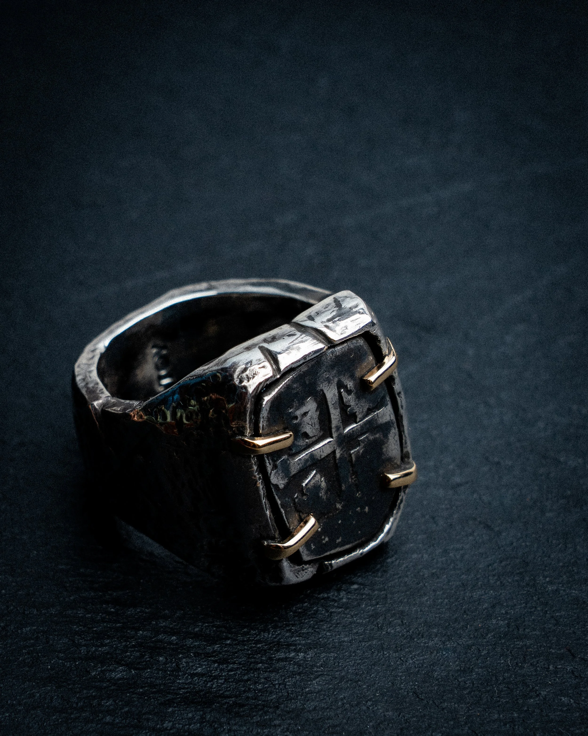 A close-up of a silver metal ring or fixture with a textured, almost patterned surface, set against a dark background.