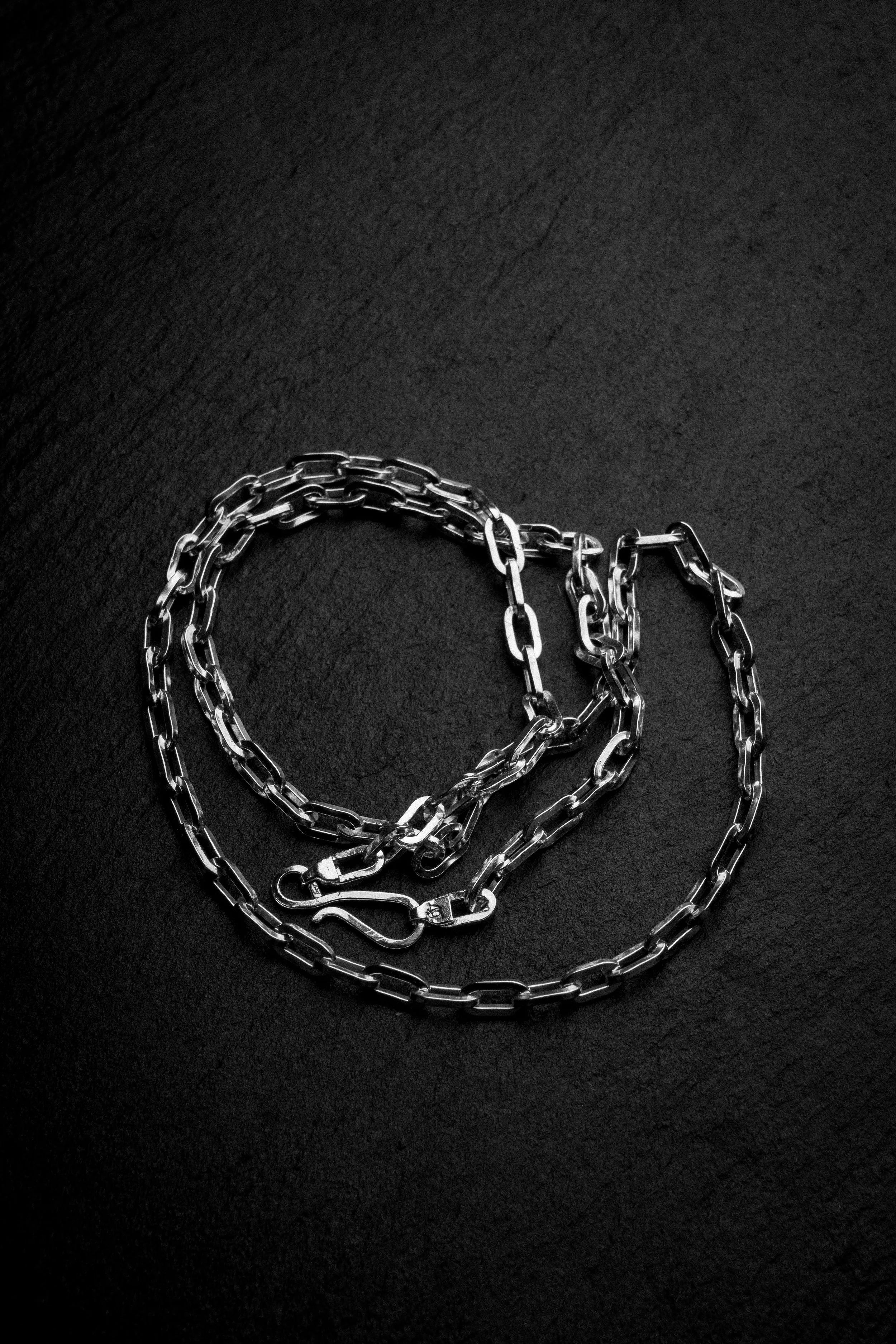 Silver chain arranged in the shape of a heart on a dark surface.