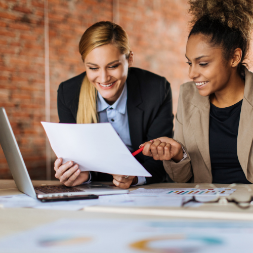 Two women reviewing documents and smiling in an office setting.