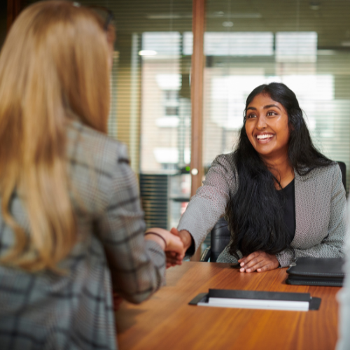 Two women shaking hands in a business meeting in an office.