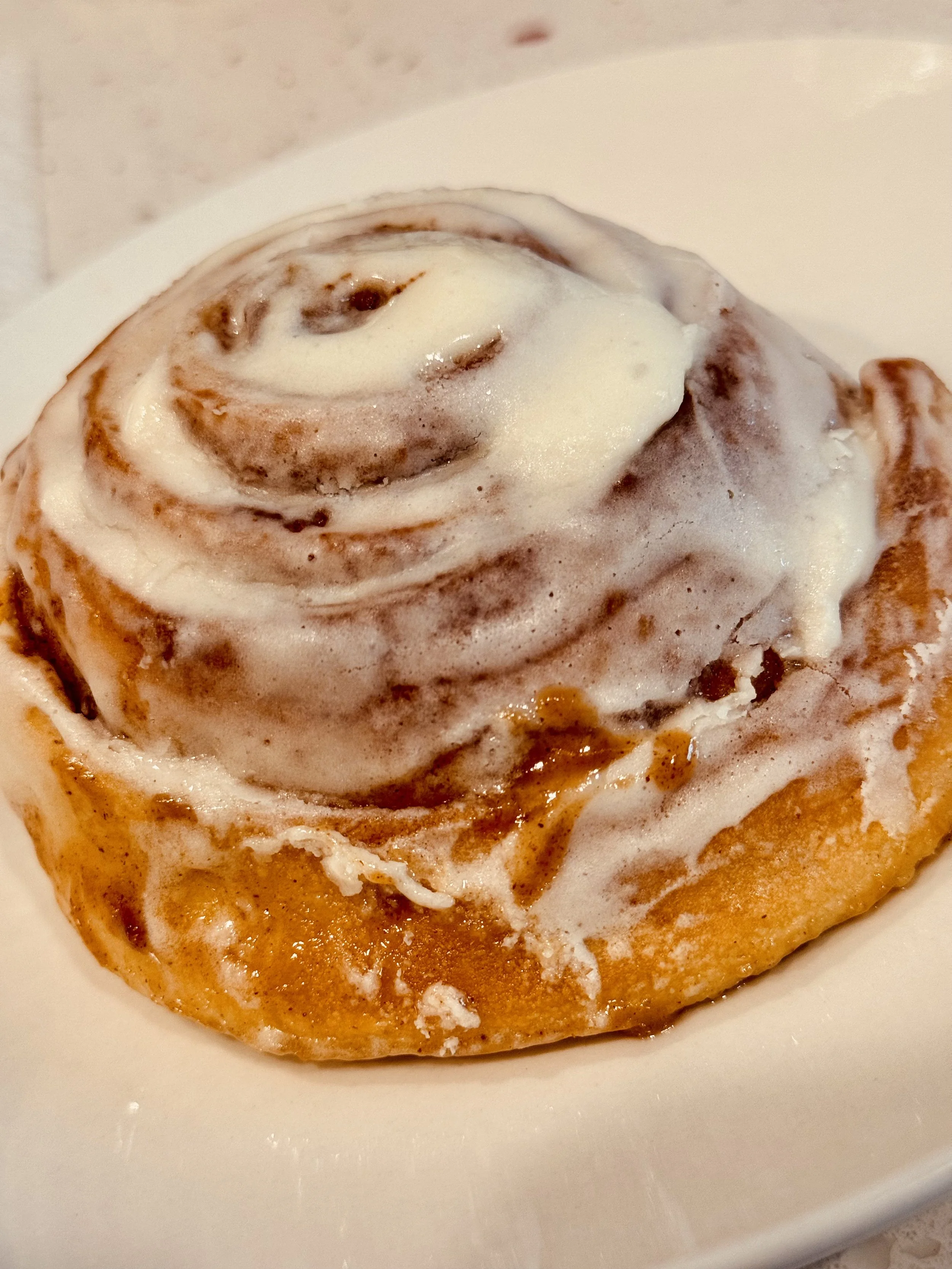 Close-up of a cinnamon roll with icing on a white plate.