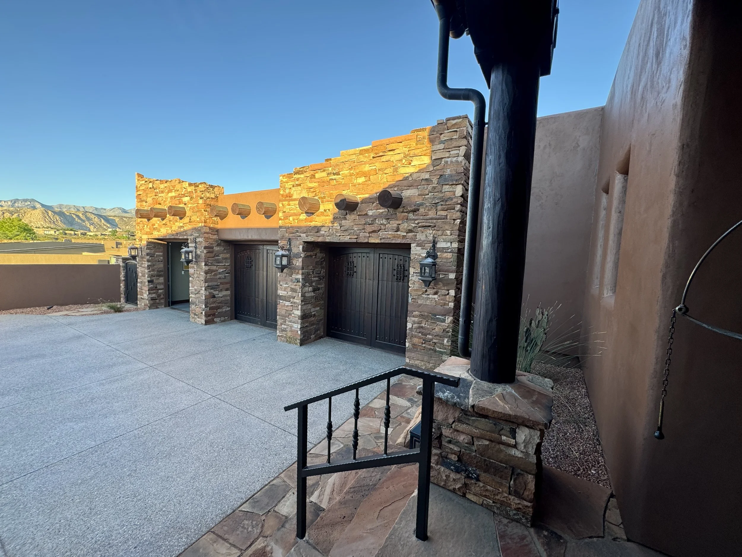 Exterior of a building with a stone facade, black garage doors, and outdoor wall-mounted lanterns, with a scenic mountain view in the background.