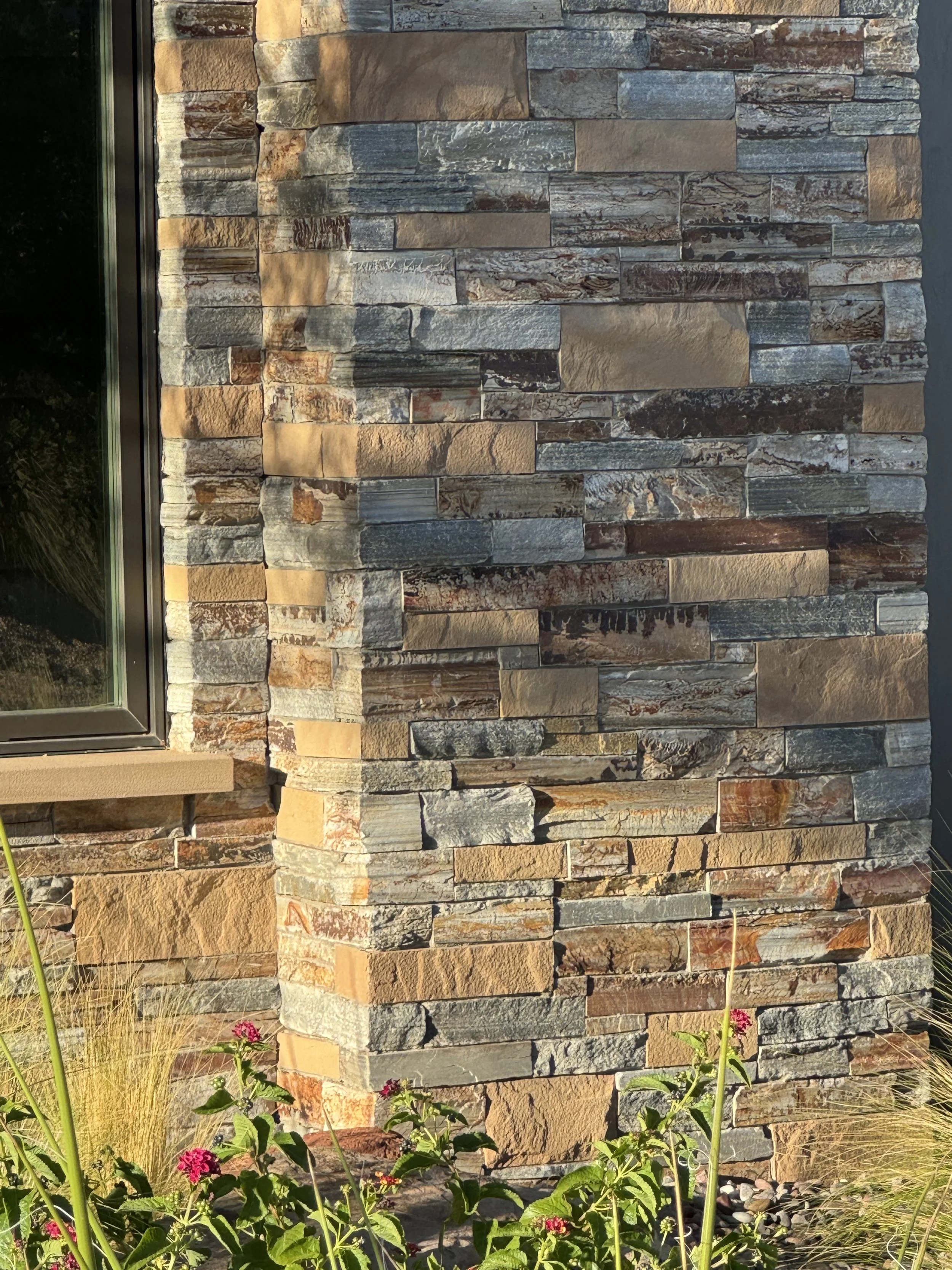 Close-up of a stone exterior wall with a window, showing various colored rectangular stones in tan, gray, and brown.