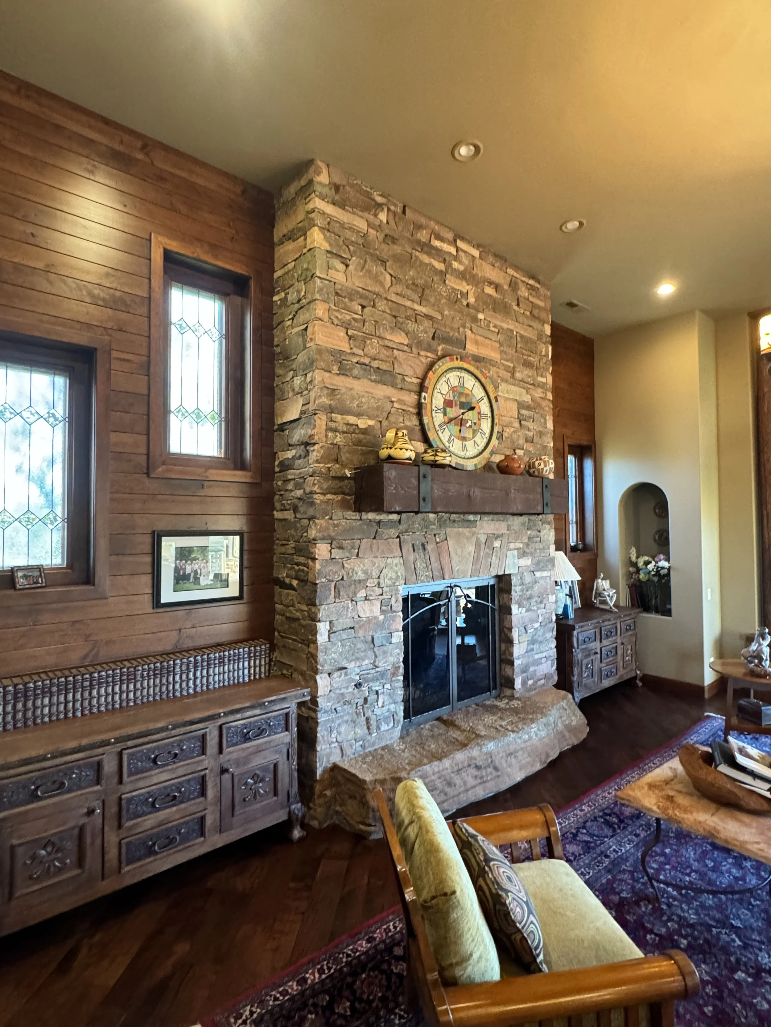 Living room with stone fireplace, wooden panel walls, and decorative items on mantel.