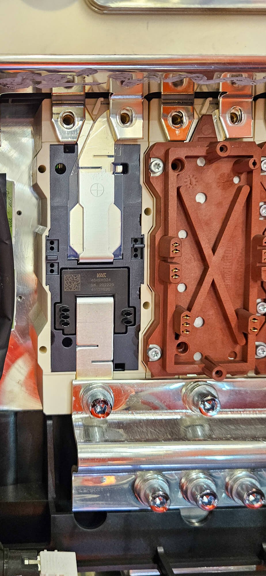 Close-up of an electronic device's internal components, including a black metal component, a red plastic part, and metal screws.