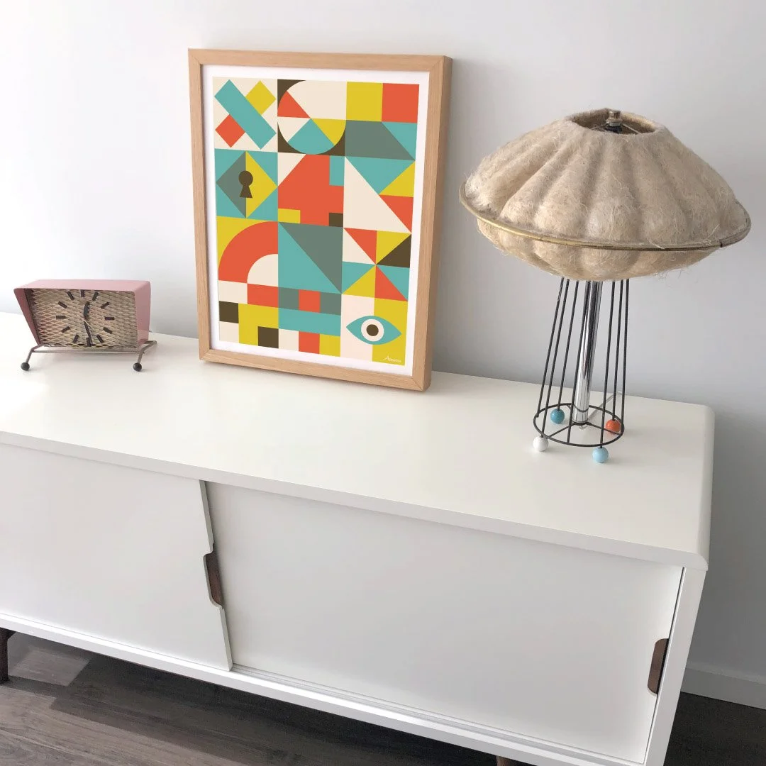 Decorative modern cabinet with colorful framed artwork, vintage clock, and a lamp with a fabric shade on top.