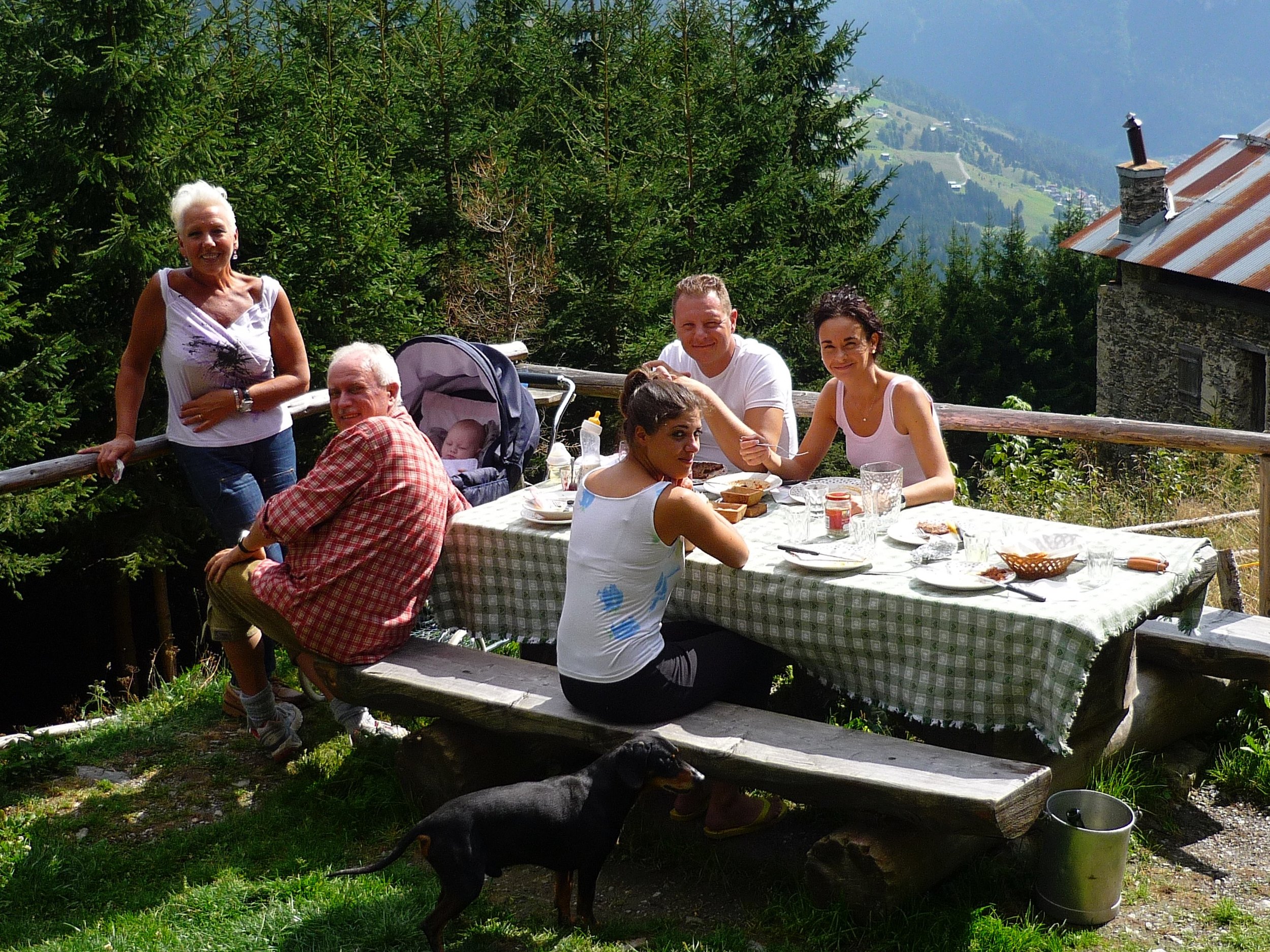 Two dark glass bottles with cork stoppers placed on a wooden barrel outdoors, with green foliage and a cloudy sky in the background.