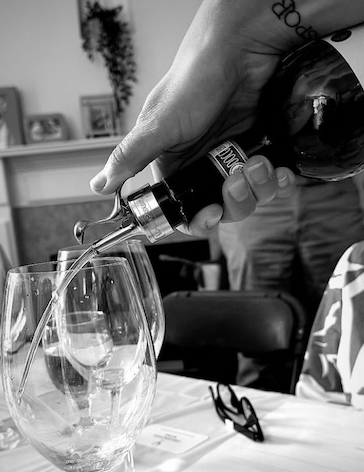 Four glasses of different colored wine on a wooden barrel, from left to right: white, rosé, red, and black.