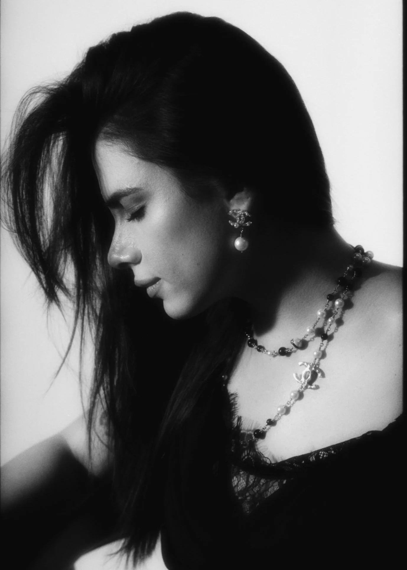 Black and white side profile of a woman with long hair, wearing pearl earrings and a necklace, with her eyes closed and head tilted downward.
