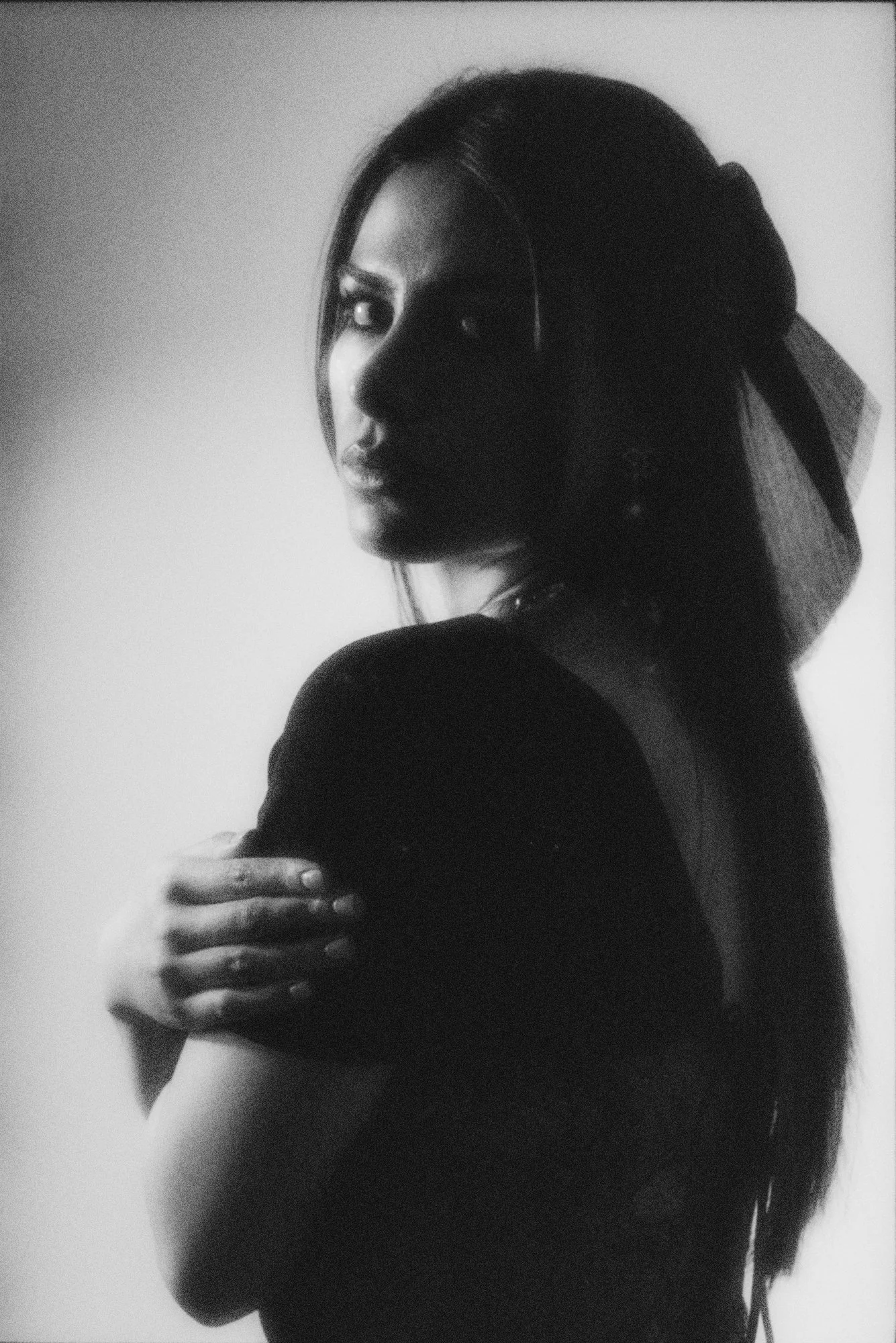 Black and white photo of a woman with long hair, looking to the side, with her arm crossed over her chest.
